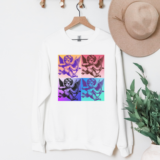 A white women's sweatshirt with a colorful pop art inspired graphic of a heart and cups on a hanger, displayed in a room setting with a hat and plant in the background.