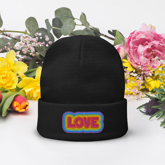 A black beanie with the word 'LOVE' embroidered in a rainbow color on the front, presented against a floral background.