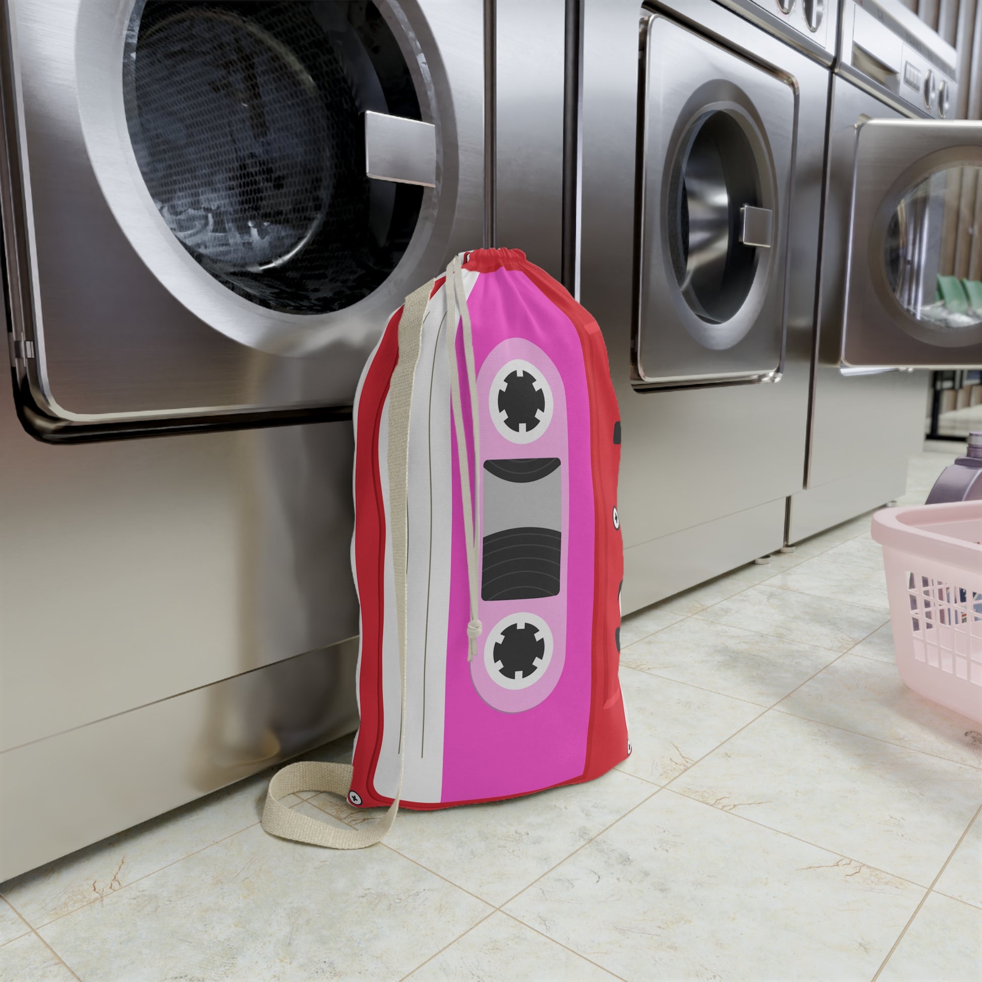 Custom laundry sack decorated with a vibrant red background, bright pink cassette tape pattern, and personalized name. The roomy 18 x 29 inch design includes a secure drawstring closure and sturdy shoulder strap for carrying clothes between bedrooms, dorm rooms, camp cabins, or laundromats. Colorful retro graphics create a playful nostalgic appearance while helping keep laundry organized and easy to transport.