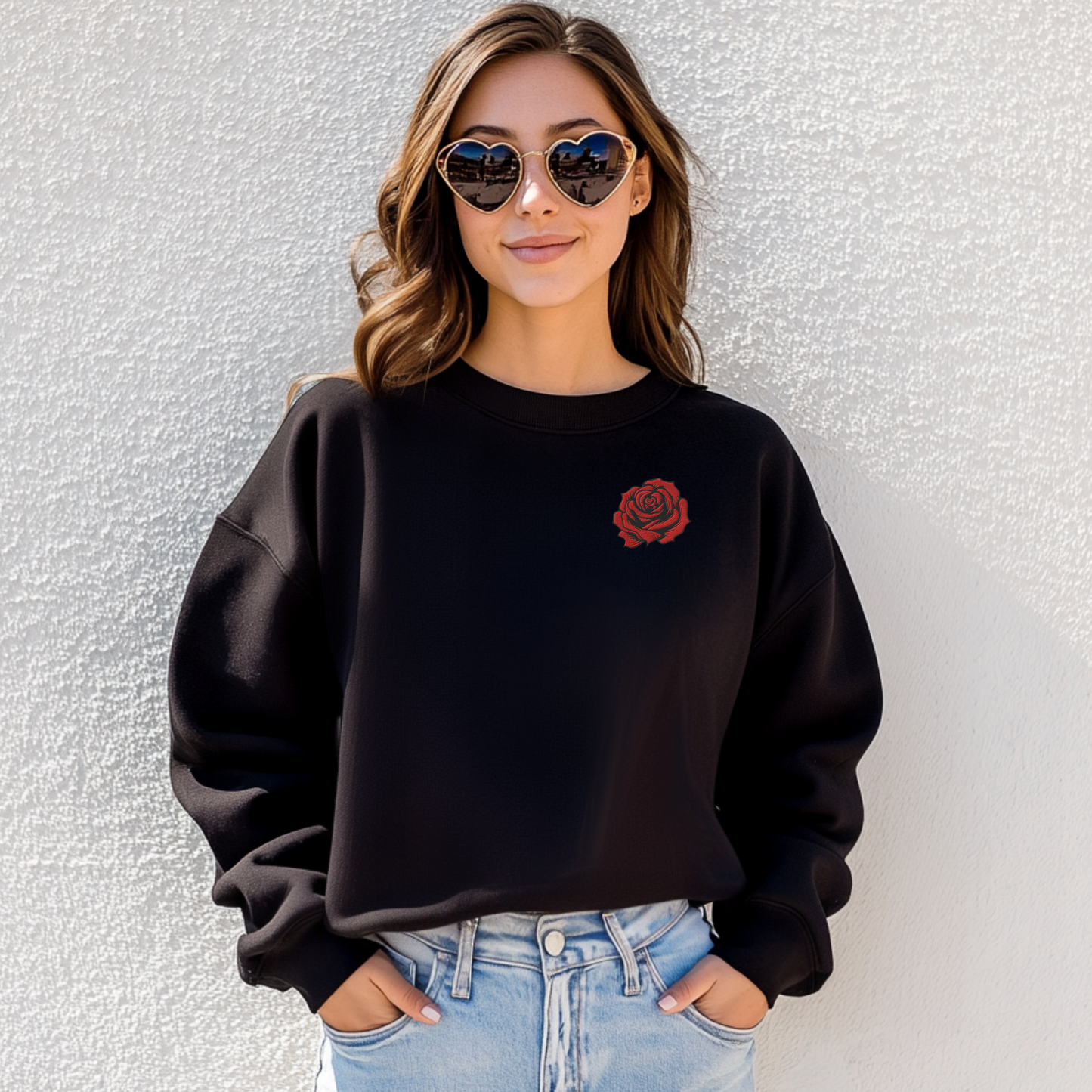 Lifestyle photo of a woman wearing a black embroidered rose sweatshirt styled casually with jeans. The bold floral embroidery adds a statement touch, while the cotton polyester blend keeps it soft and cozy. A thoughtful June birth flower gift for birthdays, anniversaries, or Valentine’s Day.