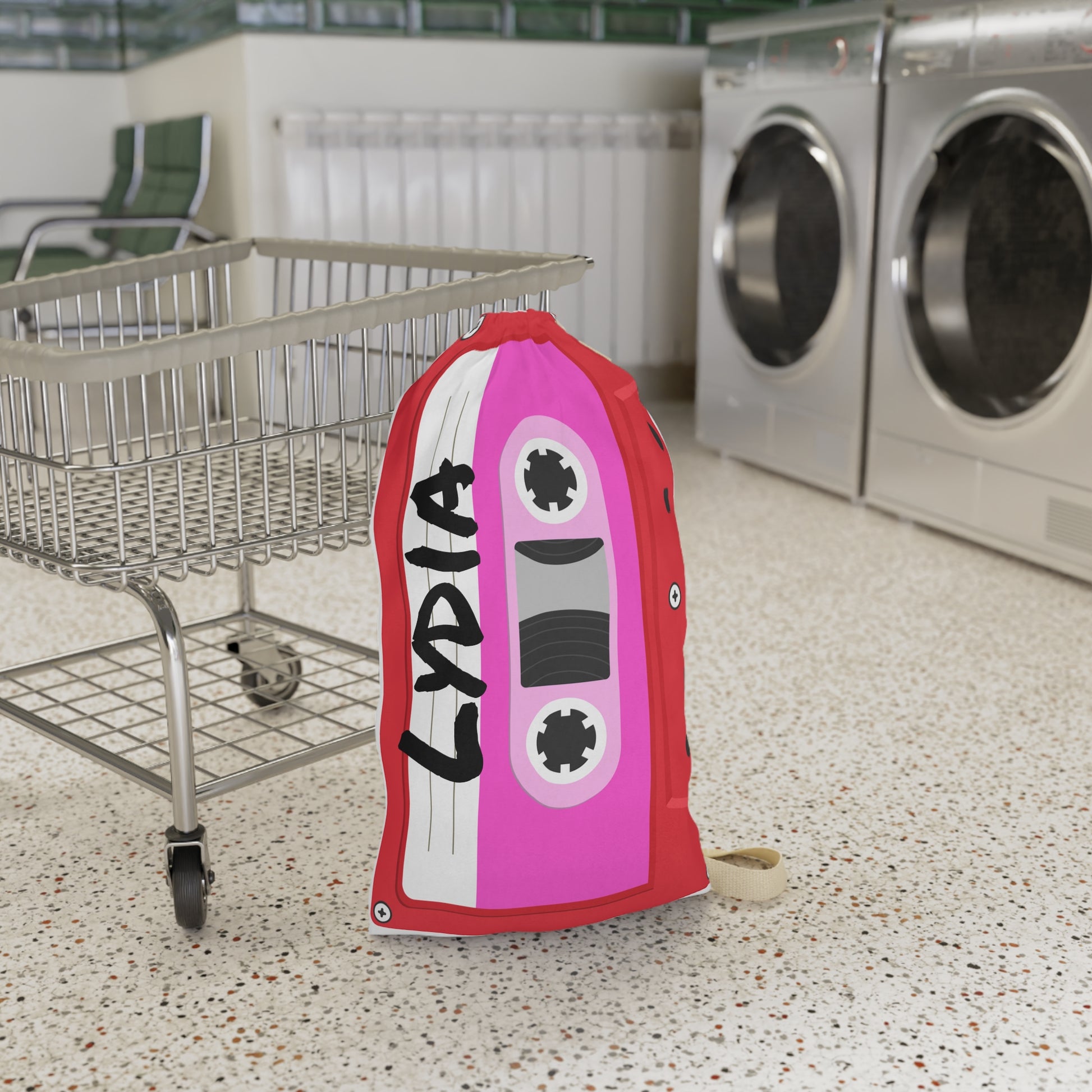 Personalized red laundry bag featuring colorful cassette tape illustrations accented with bright pink details and a custom name printed across the fabric. The 18 x 29 inch bag includes a drawstring closure at the top and a woven shoulder strap for convenient carrying. Retro music inspired artwork covers the surface, creating a fun vintage look. Spacious design provides room for clothing, towels, bedding, and camp essentials while adding personality to everyday organization.