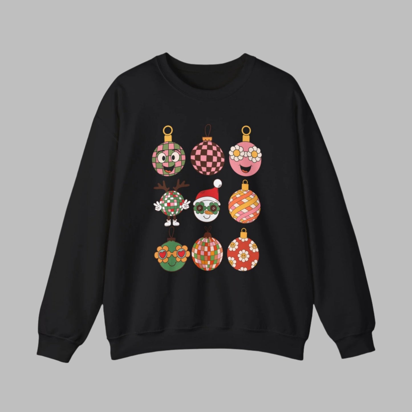 Festive Retro Christmas Ornament Sweatshirt in light pink, black, or sand, featuring nine cartoon ornaments with checkerboard, floral, and retro Santa designs. This cozy Gildan 18000 crewneck is soft, durable, and available in sizes S–5XL, making it a perfect Christmas outfit for holiday parties, family gatherings, or fun vintage-inspired photos. A great holiday gift for retro fashion lovers who want a unique and groovy Christmas pullover.