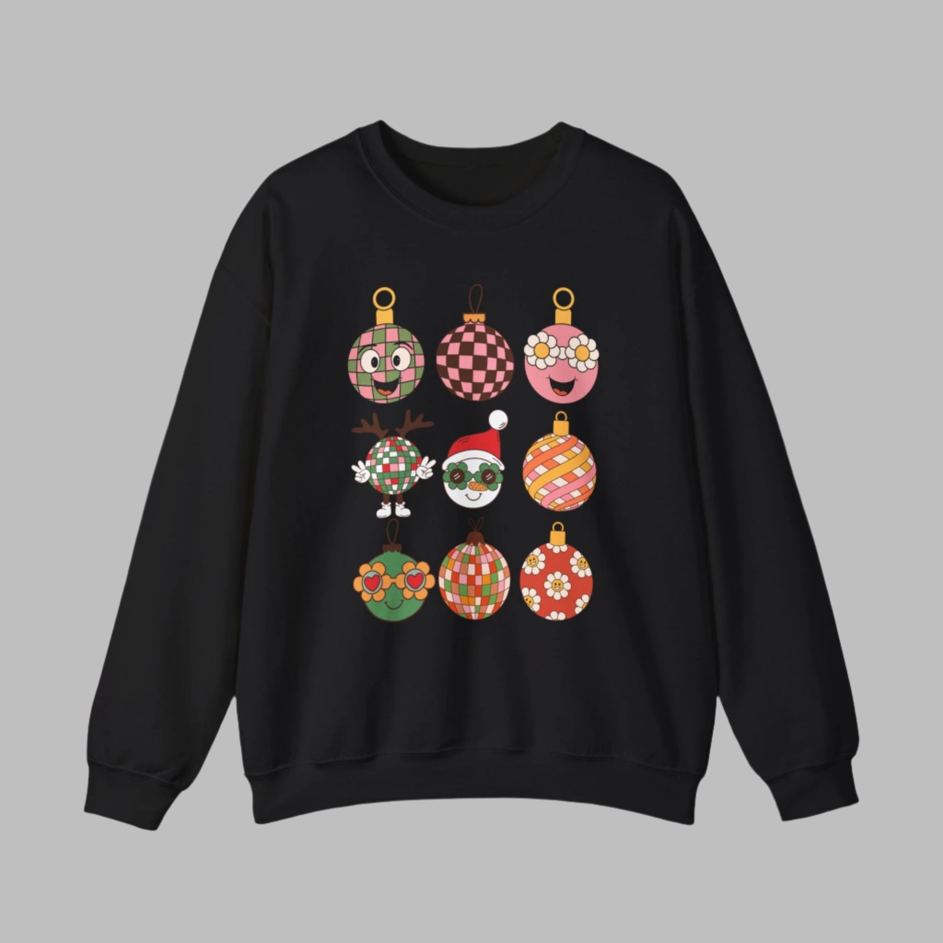 Festive Retro Christmas Ornament Sweatshirt in light pink, black, or sand, featuring nine cartoon ornaments with checkerboard, floral, and retro Santa designs. This cozy Gildan 18000 crewneck is soft, durable, and available in sizes S–5XL, making it a perfect Christmas outfit for holiday parties, family gatherings, or fun vintage-inspired photos. A great holiday gift for retro fashion lovers who want a unique and groovy Christmas pullover.