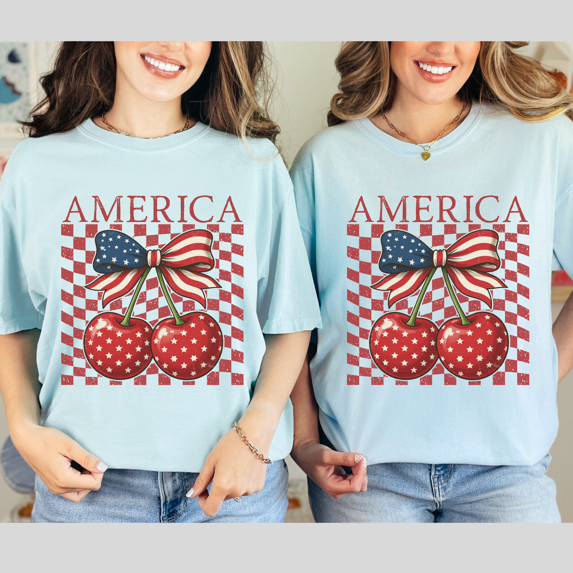 Two women weating the retro Americana Comfort Colors shirt featuring playful cherry coquette design. America text crowns two bright cherries decorated in white stars and connected by a large flag inspired bow. Distressed checkerboard backdrop gives classic summer race track vibes with a boutique look. Relaxed cotton tee with soft garment dyed texture for all day comfort. Perfect for Fourth of July parties, beach boardwalk nights, county fairs, and patriotic photo shoots.