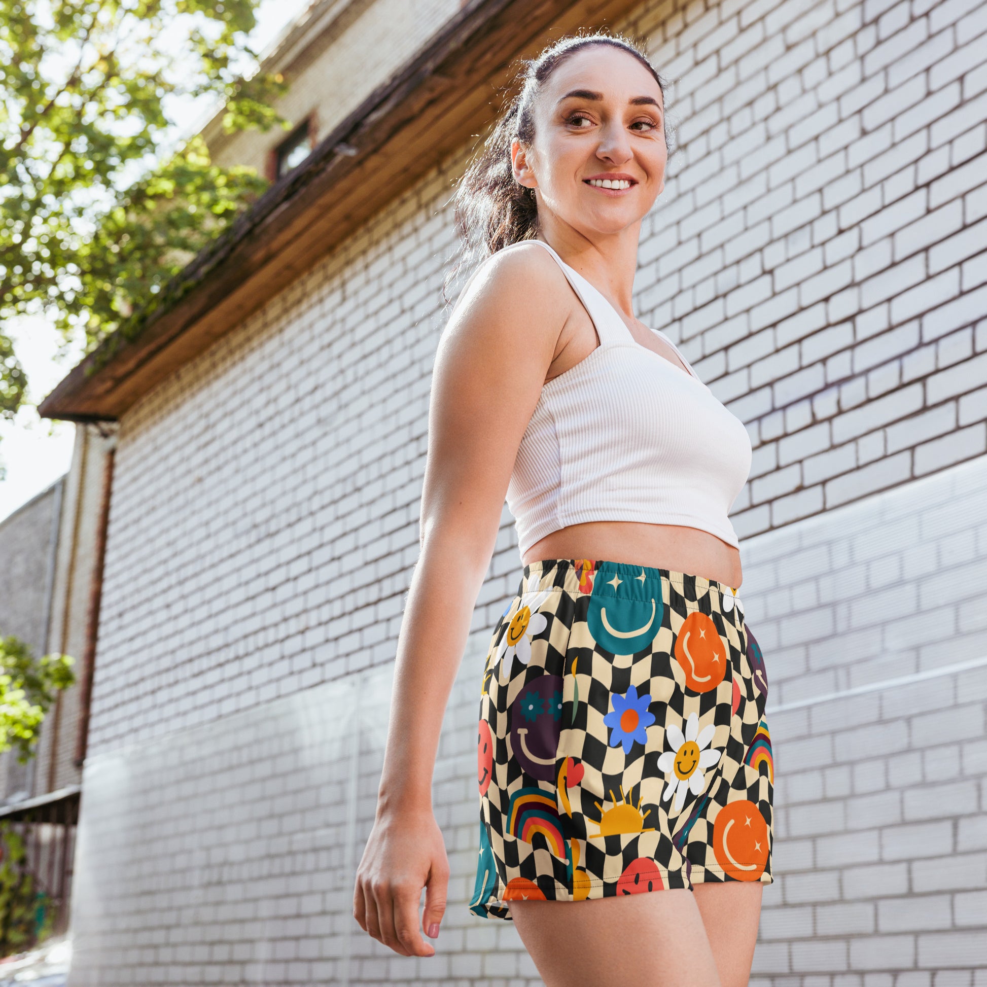 Smiley face checkerboard athletic shorts featuring a retro beige and black wavy checker pattern with playful smiley face accents, designed as unisex workout shorts with a comfortable elastic waistband and flat white drawstring. These breathable athletic shorts are made from moisture wicking recycled polyester fabric with four way stretch, mesh side pockets, and a 2.5 inch inseam, making them perfect for gym workouts, sports, running, lounging, and casual athleisure wear, available in inclusive sizes XS to 3