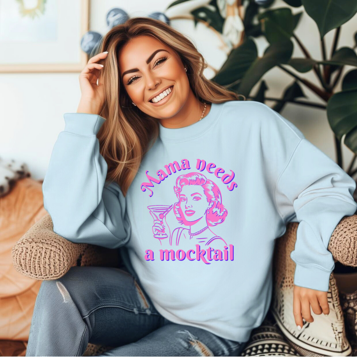 Woman wearing a light blue Comfort Colors sweatshirt with a colorful retro pop art graphic that reads “Mama Needs a Mocktail.” The vintage inspired illustration features a woman holding a cocktail glass and uses bright pink and blue tones for a bold statement. The relaxed sweatshirt pairs easily with casual bottoms for brunch, weekends, girls nights, or everyday wear and makes a fun choice for mocktail loving moms.