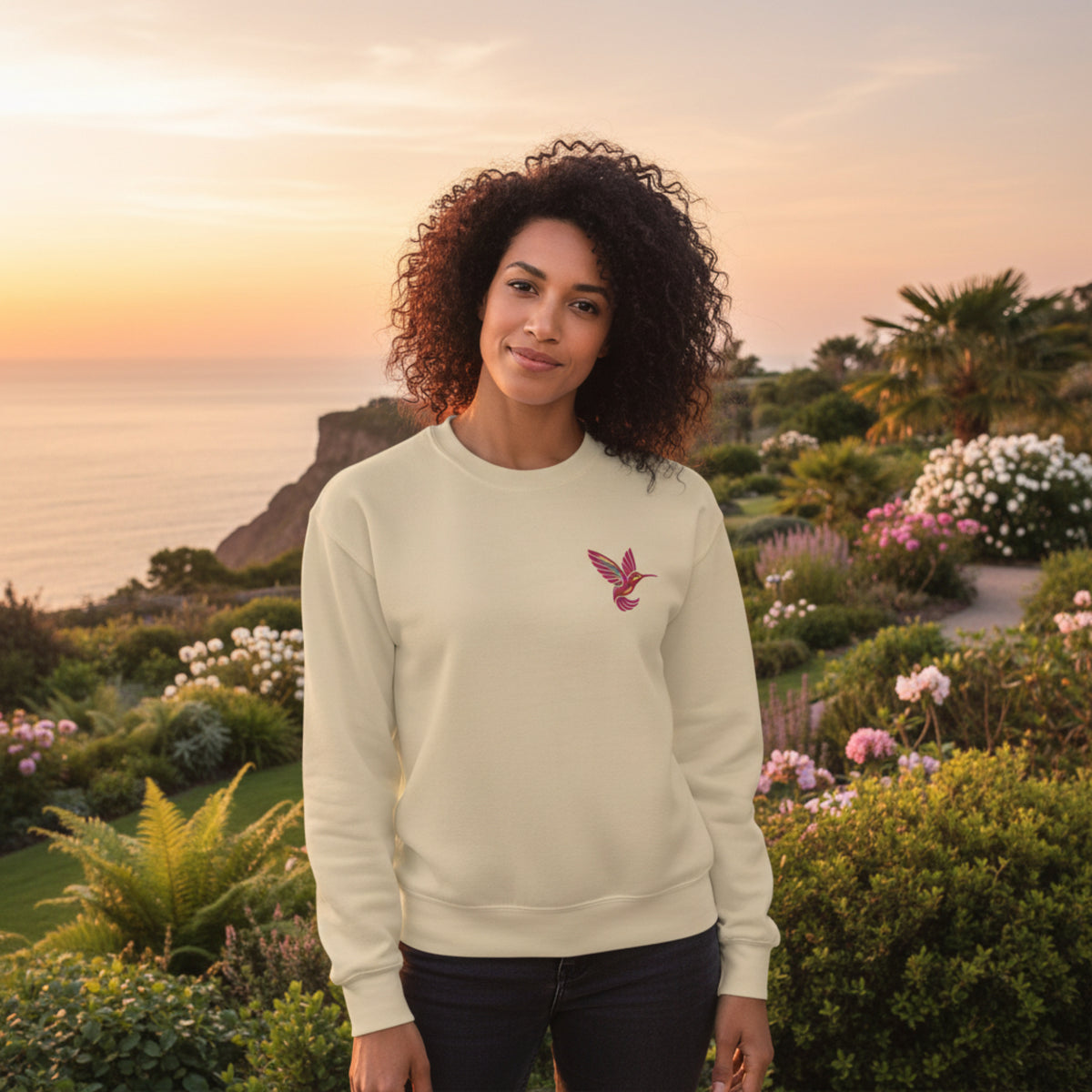 Sand colored Gildan crewneck sweatshirt featuring a colorful embroidered hummingbird on the chest. The warm neutral sweatshirt color pairs naturally with the vibrant bird embroidery for a relaxed, nature inspired look. This comfortable everyday sweatshirt can be styled with jeans, leggings, or layered outfits and makes a thoughtful option for bird lovers, gardeners, nature enthusiasts, or anyone who appreciates colorful embroidered details.