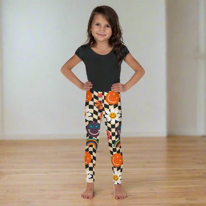 Playful and stylish, these Smiley Face Checkerboard Girls Leggings in toddler and little girl sizes 2T–7 feature a beige and black wavy checkerboard design with daisies, rainbows, and smiley faces. Made with a soft polyester-spandex blend, these leggings keep kids comfortable and active all day. Available in coordinating youth and women’s sizes for matching family looks, gifts, or sibling photo outfits.
