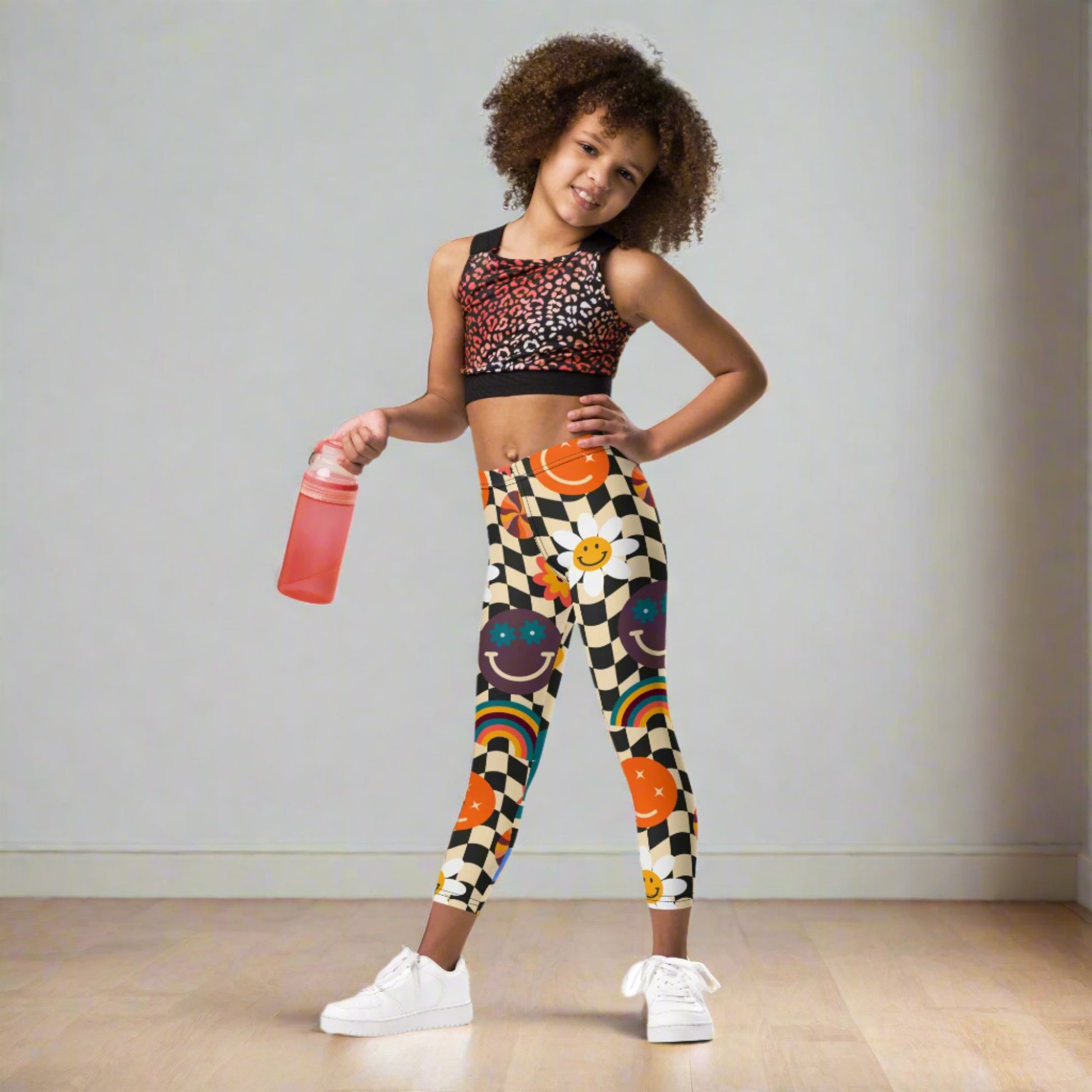 Add happiness to her wardrobe with Smiley Face Checkerboard Girls Leggings in toddler and little girl sizes 2T–7. The beige and black wavy checkerboard pattern is accented with cheerful daisies, colorful rainbows, and smiley faces. Perfect for play or casual wear, these leggings are soft, durable, and fade-resistant. Matching youth and women’s sizes make them a fun family outfit idea for group photos and seasonal celebrations.