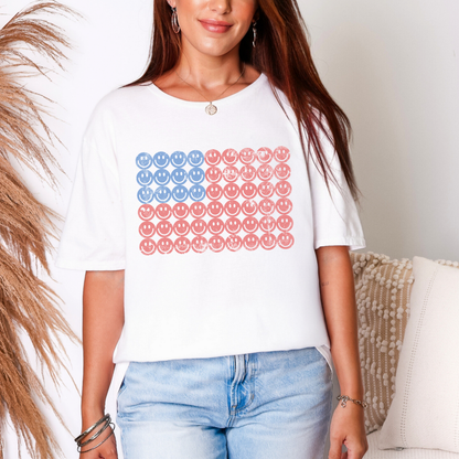 Woman wearing a smiley face American flag t shirt with a red white and blue graphic design, cute patriotic unisex tee outfit for 4th of July celebrations, summer events, and casual everyday wear