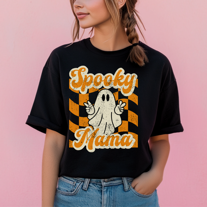 Black Spooky Mama Halloween shirt featuring a cute ghost giving peace signs over an orange checkered background, printed on a soft Gildan 64000 Softstyle tee. Fun spooky season graphic shirt for moms who love playful fall style. Lightweight comfortable tshirt perfect for pumpkin patch visits, trick or treat nights, school parties, hayrides, coffee runs, and cozy autumn weekends. Pairs with jeans or leggings and coordinates with matching Spooky Mini kids shirt. Free U.S. Shipping.
