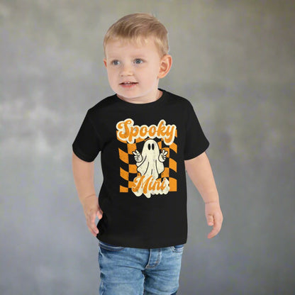 Adorable Spooky Mini toddler Halloween shirt featuring cute ghost with peace sign hand gesture on orange checkered retro style background printed on Bella Canvas 3001T cotton tee. Designed for comfort and style during fall season activities including pumpkin patch visits, Halloween parties, school events, and trick or treating. Soft fabric makes it perfect for toddlers, and matching Spooky Mama shirt completes family coordinated outfits.