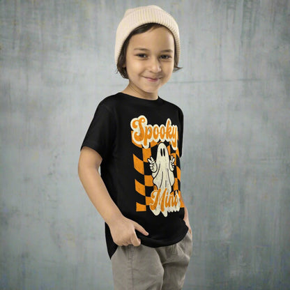Halloween toddler shirt featuring Spooky Mini ghost graphic with peace sign over retro orange checkered background design printed on a soft Bella Canvas 3001T cotton tee. Perfect for spooky season outfits, trick or treating, pumpkin patch photos, school celebrations, and fall family events. Lightweight and breathable for comfort all day long. Matching Mama and Mini tees available featuring coordinating Spooky Mama design for family matching looks.