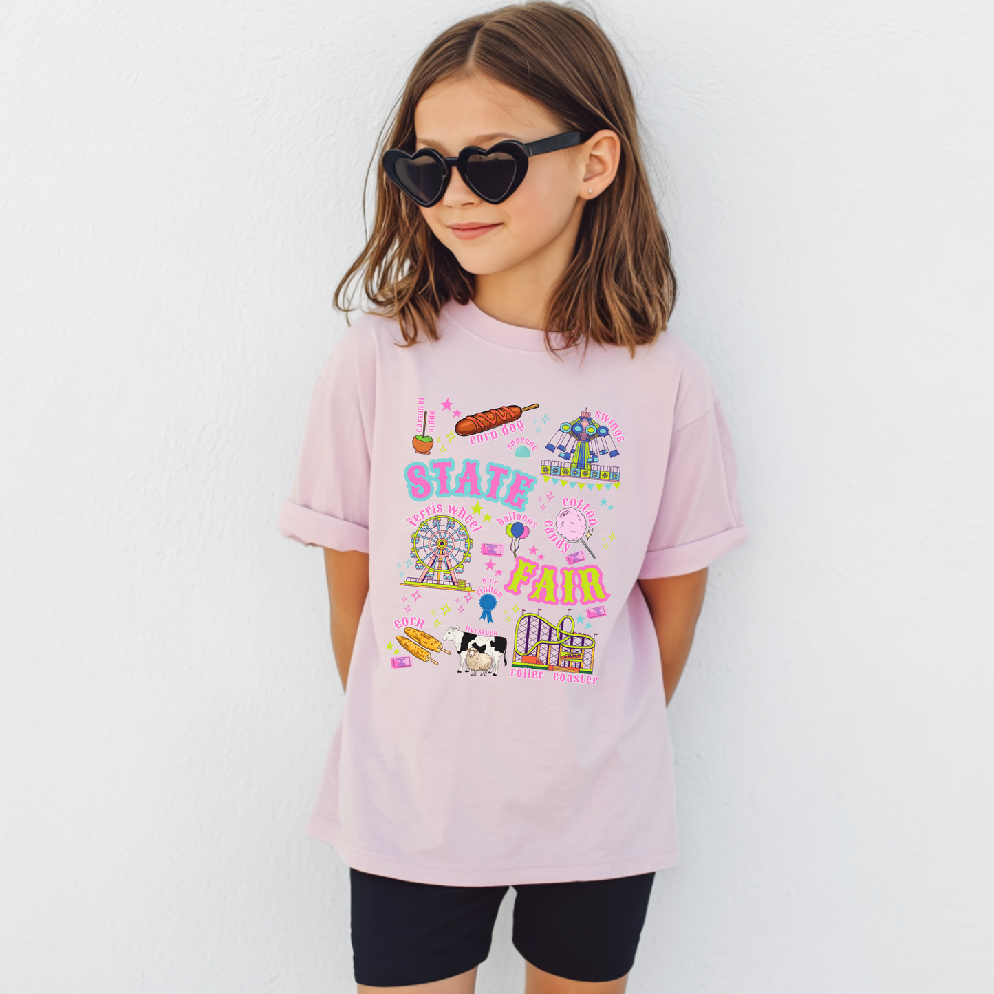 Youth State Fair graphic T shirt featuring colorful carnival and county fair artwork with Ferris wheel, roller coaster, swing ride, cotton candy, funnel cake, corn dogs, balloons, livestock and blue ribbon illustrations. Retro lettering and bright colors create a playful fair day look for kids.

