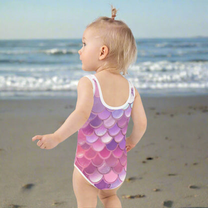Back view of a toddler wearing JaeCrece’s Mermaid One-Piece Swimsuit in size 2T–7, showing the vibrant pink, purple, blue, and white mermaid scales print. The swimsuit’s smooth microfiber yarn and four-way stretch fabric provide a comfortable fit, while UPF 38–40 protection helps keep little ones safe during sunny outdoor water activities and poolside adventures.