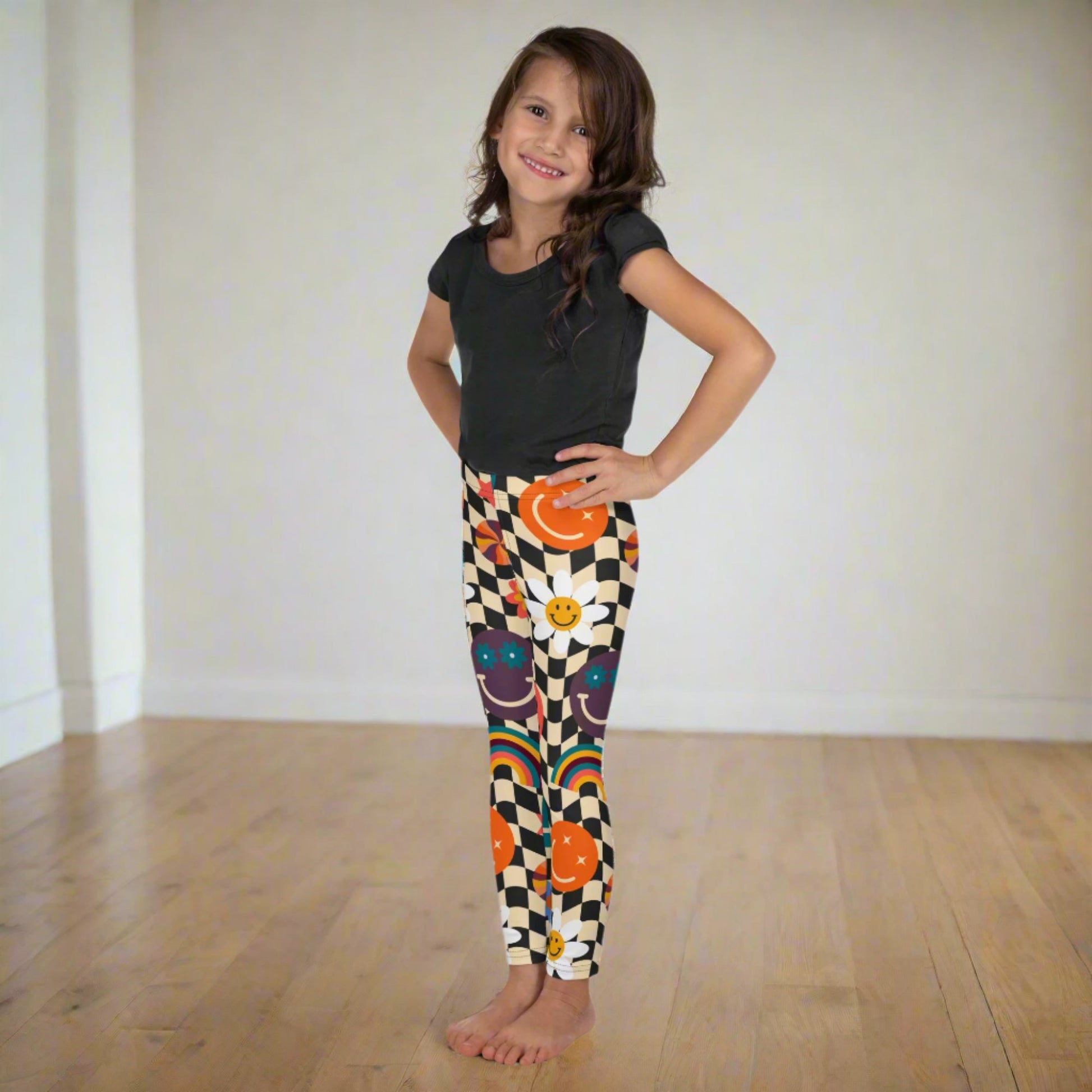 Toddler and little girl Smiley Face Checkerboard Leggings in sizes 2T–7 feature a fun beige and black checkerboard print with wavy lines, bright rainbows, smiley faces, and daisies. These playful leggings combine comfort with durability, making them ideal for school, play, or lounging. Coordinating leggings in youth and women’s sizes make them a great family matching outfit option for special occasions and everyday fun.