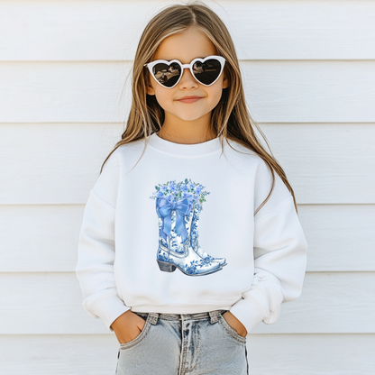 Girl wearing a white Blue Toile Boots sweatshirt with a blue floral cowboy boot design across the front. This feminine Western inspired girls sweatshirt combines a classic blue and white color palette with country charm, making it perfect for everyday outfits, school and casual occasions.