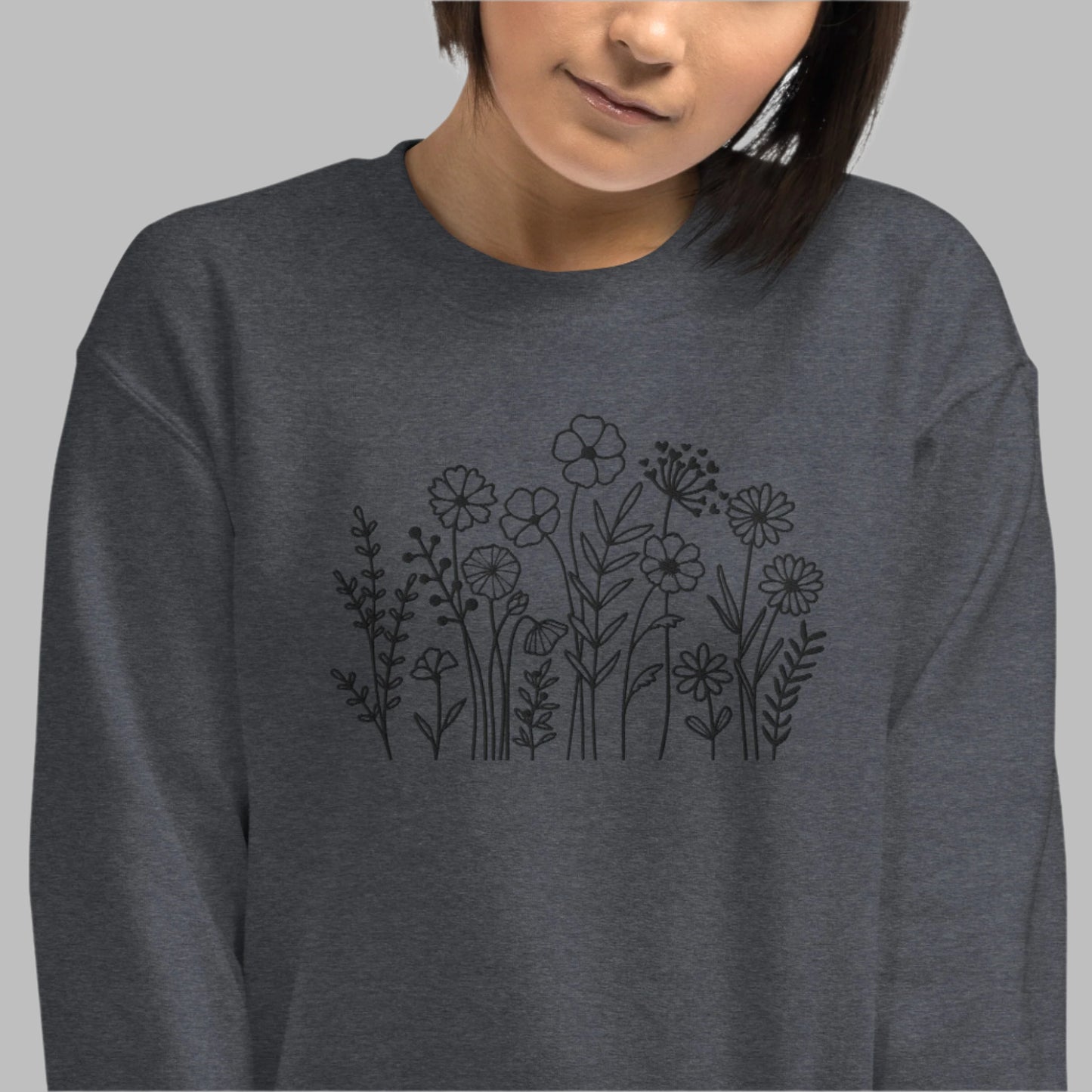 Image: A cozy dark grey sweatshirt with delicate black wildflower embroidery across the chest, showcasing a minimalist yet elegant botanical design. The soft fabric drapes effortlessly, offering comfort for everyday wear. This floral nature crewneck is perfect for layering, adding a subtle floral charm to casual outfits. A thoughtful gift for plant lovers or those who appreciate nature-inspired fashion, by jaecrece.