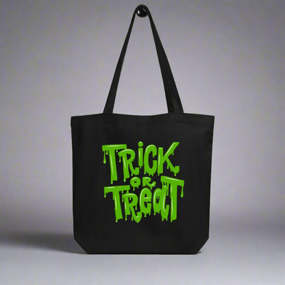 Reusable Trick or Treat Tote Bag with green ooze lettering, printed on black organic cotton. Designed for eco-friendly trick-or-treating, this Halloween candy bag is durable, holds up to 30 lbs, and makes a sustainable alternative to disposable bags. Perfect for kids and adults, this versatile tote doubles as a spooky everyday bag, Halloween party favor, or gift for families who want practical style during spooky season.
