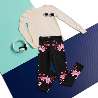 Flatlay of black cherry blossom leggings featuring delicate pink sakura flowers and graceful flowering branches, highlighting the full length design and feminine Japanese inspired floral pattern. These high rise leggings are designed for tween and teen girls and can be styled as everyday leggings or yoga pants with casual tops, sweatshirts, sweaters, and spring outfits.