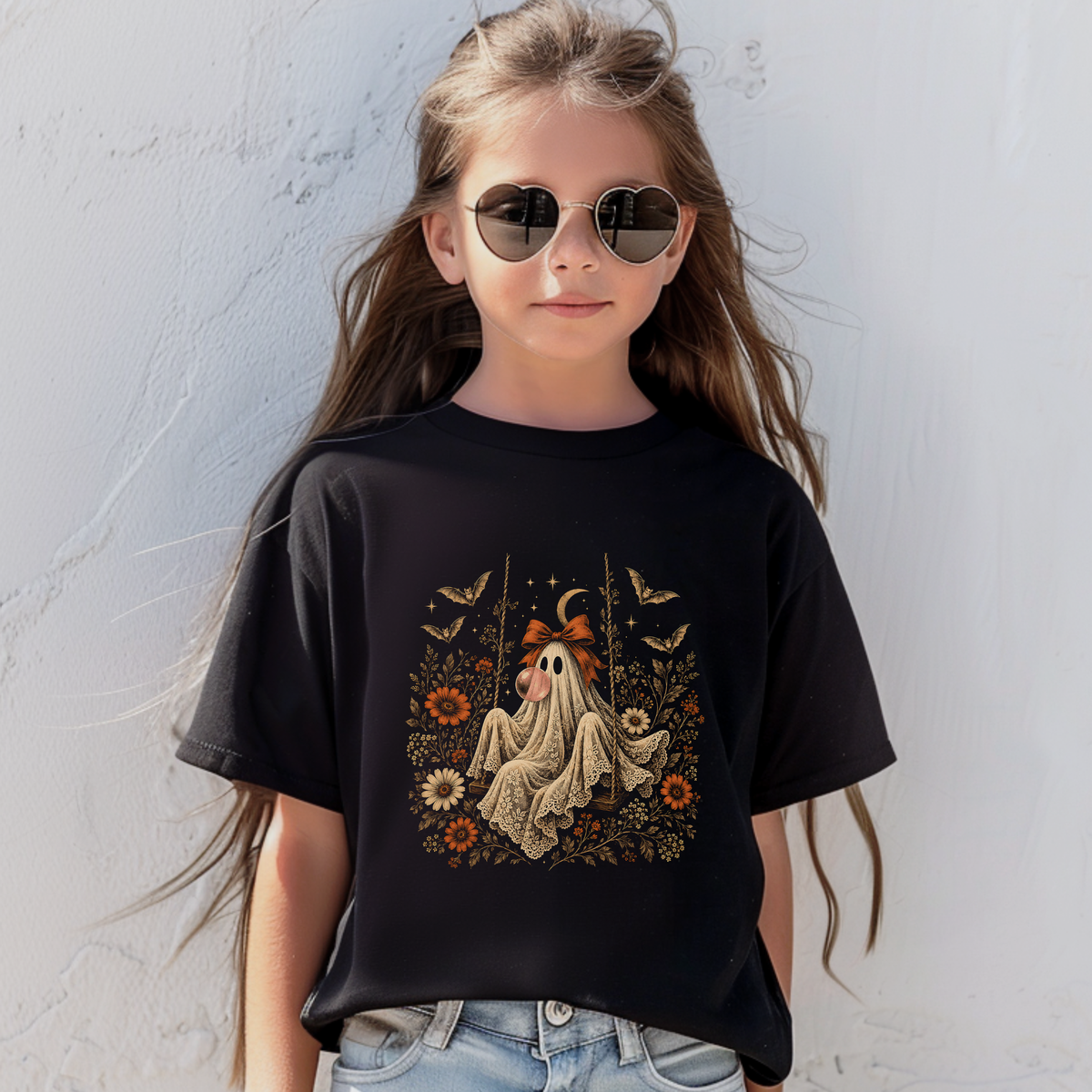 whimsical Halloween graphic tshirt featuring a vintage inspired ghost blowing a bubble with bubble gum, surrounded by orange flowers, botanical foliage, bats, stars, lace details and a bow. The playful ghost artwork gives this girls graphic tee a distinctive vintage spooky season look.