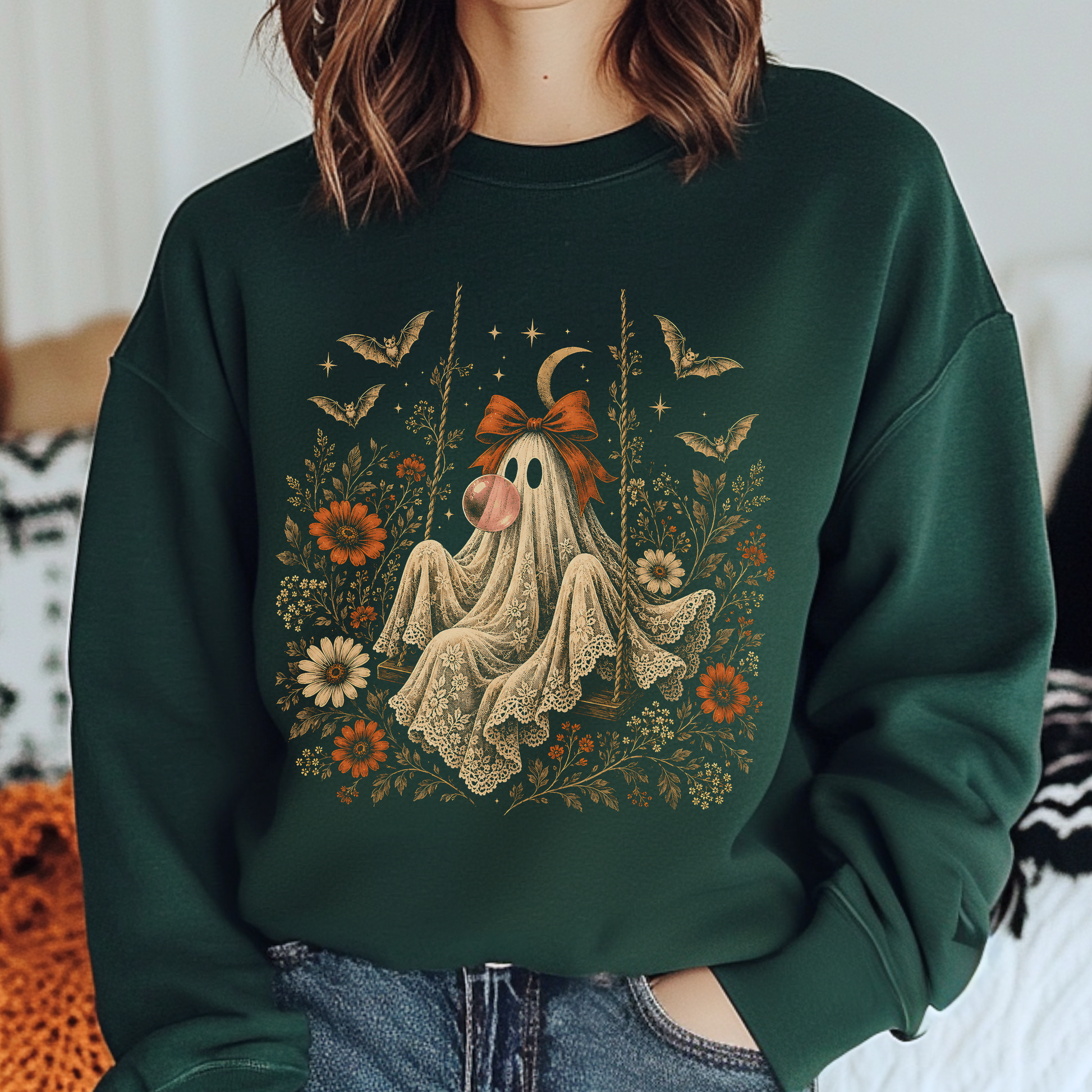 Vintage Halloween crewneck featuring a ghost on a swing blowing bubble gum beneath a crescent moon. The detailed artwork includes flowers, leaves, bats, lace and stars, creating a whimsical spooky design that works beautifully for fall outfits and Halloween gatherings.
