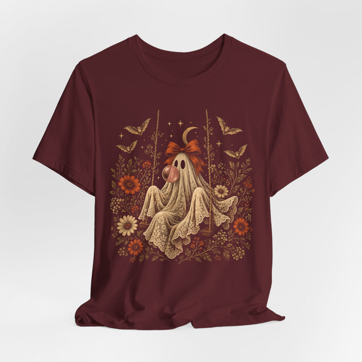 Vintage Halloween graphic tee featuring a ghost on a swing blowing bubble gum beneath a crescent moon. The detailed artwork includes flowers, leaves, bats, lace and stars, creating a whimsical spooky design for fall outfits and Halloween gatherings.