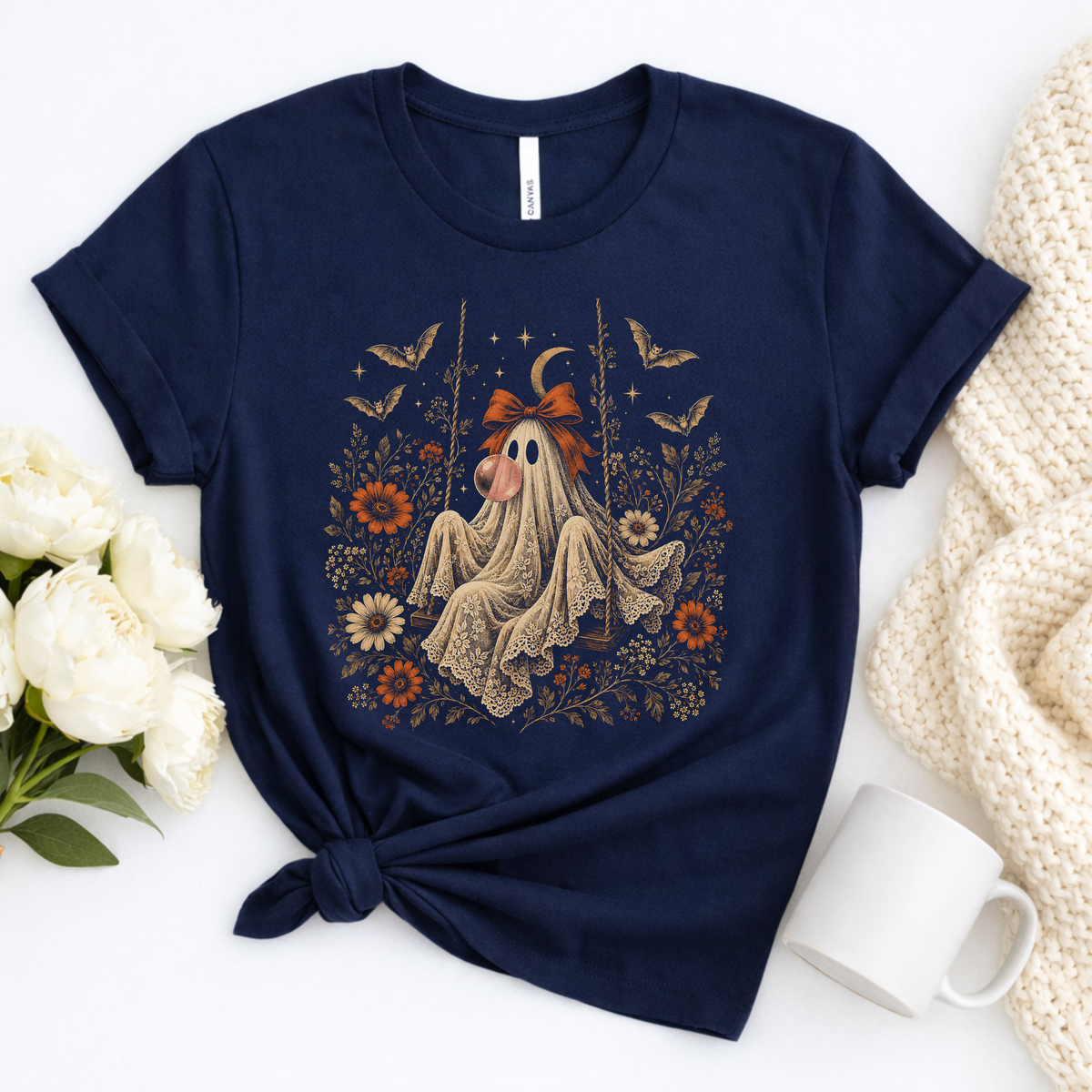 Vintage Halloween shirt for women featuring a whimsical ghost sitting on a swing while blowing a bubble with bubble gum. The artwork includes vintage flowers, botanical foliage, bats, lace, stars and a crescent moon for a detailed spooky season design