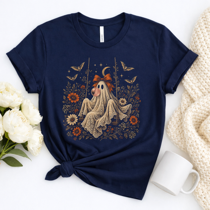 Vintage Halloween shirt for women featuring a whimsical ghost sitting on a swing while blowing a bubble with bubble gum. The artwork includes vintage flowers, botanical foliage, bats, lace, stars and a crescent moon for a detailed spooky season design