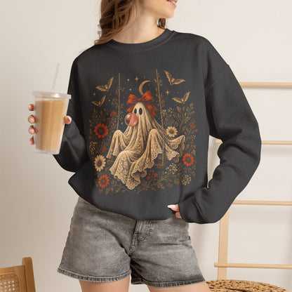 A woman wearing a dark charcoal gray crewneck sweatshirt with a detailed graphic of a ghost on a swing surrounded by autumn leaves and flowers. Vintage Halloween graphic sweater for women featuring a whimsical ghost sitting on a swing while blowing a bubble with bubble gum, surrounded by vintage flowers, botanical elements, bats, lace, stars and a crescent moon in a detailed autumn inspired design.