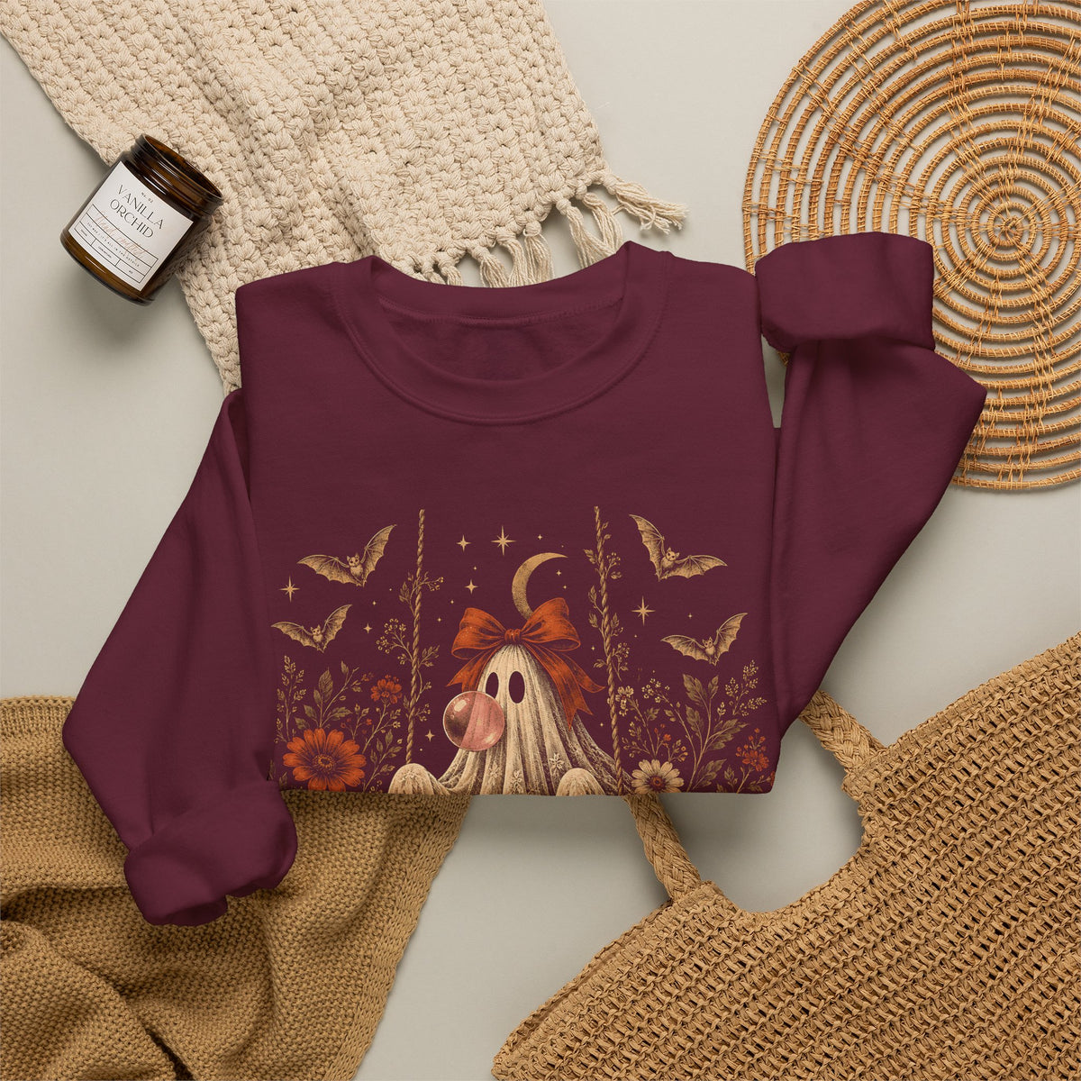 Vintage Halloween sweatshirt featuring a whimsical ghost sitting on a swing while blowing a bubble with bubble gum. The artwork includes vintage flowers, botanical foliage, bats, lace, stars and a crescent moon for a detailed spooky season design.