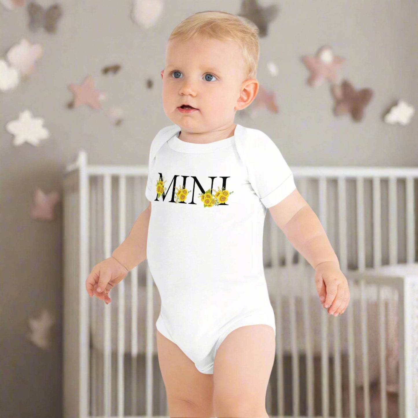 Soft and stylish Mini Sunflower Baby Bodysuit for newborns and toddlers, available in White or Pink Bella Canvas 100B. Features sunflower “MINI” calligraphy and coordinates with MAMA sweatshirt and tee for family matching outfits. Comfortable, breathable, and easy to wear with a three-snap closure and envelope neckline, this baby bodysuit is perfect for everyday wear, gifting, and creating memorable family photo moments.