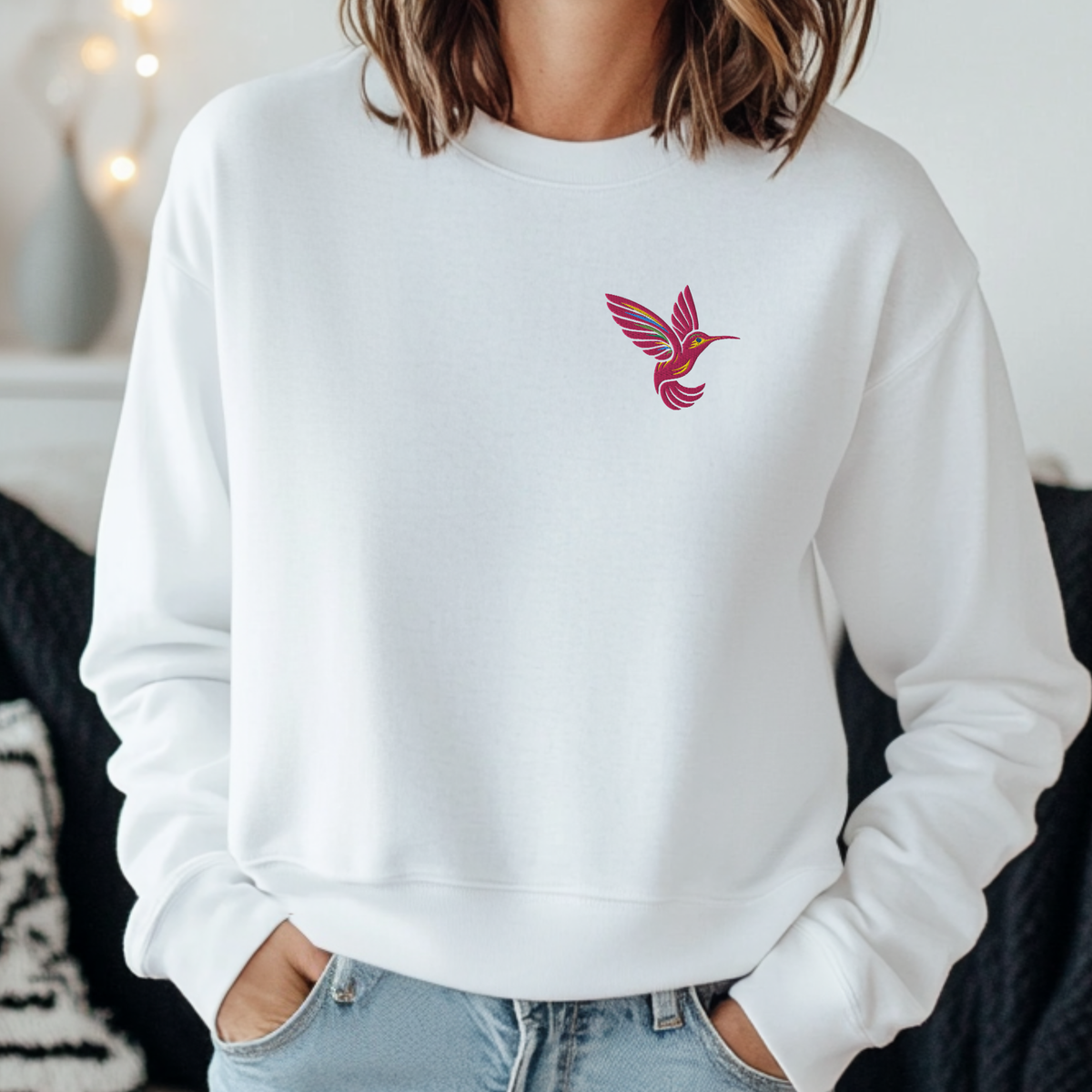 White Gildan 18000 crewneck sweatshirt with a colorful embroidered hummingbird positioned on the chest. The light background of the sweatshirt creates a clean contrast with the detailed bird embroidery and gives the design a simple, delicate appearance. White is an easy neutral to style with jeans, leggings, shorts, or casual layers, making this hummingbird sweatshirt a versatile choice for everyday wear.