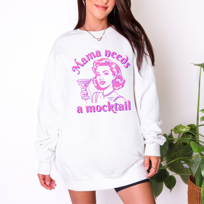 Woman wearing a white oversized Comfort Colors crewneck sweatshirt featuring the colorful “Mama Needs a Mocktail” retro pop art graphic. The relaxed oversized fit gives the sweatshirt a casual, effortless look while the bold pink and blue illustration adds a playful vintage inspired statement. This cozy style is perfect for lounging, brunch, girls nights, casual weekends, or anyone who loves mocktails, alcohol free drinks, and fun mom themed clothing.