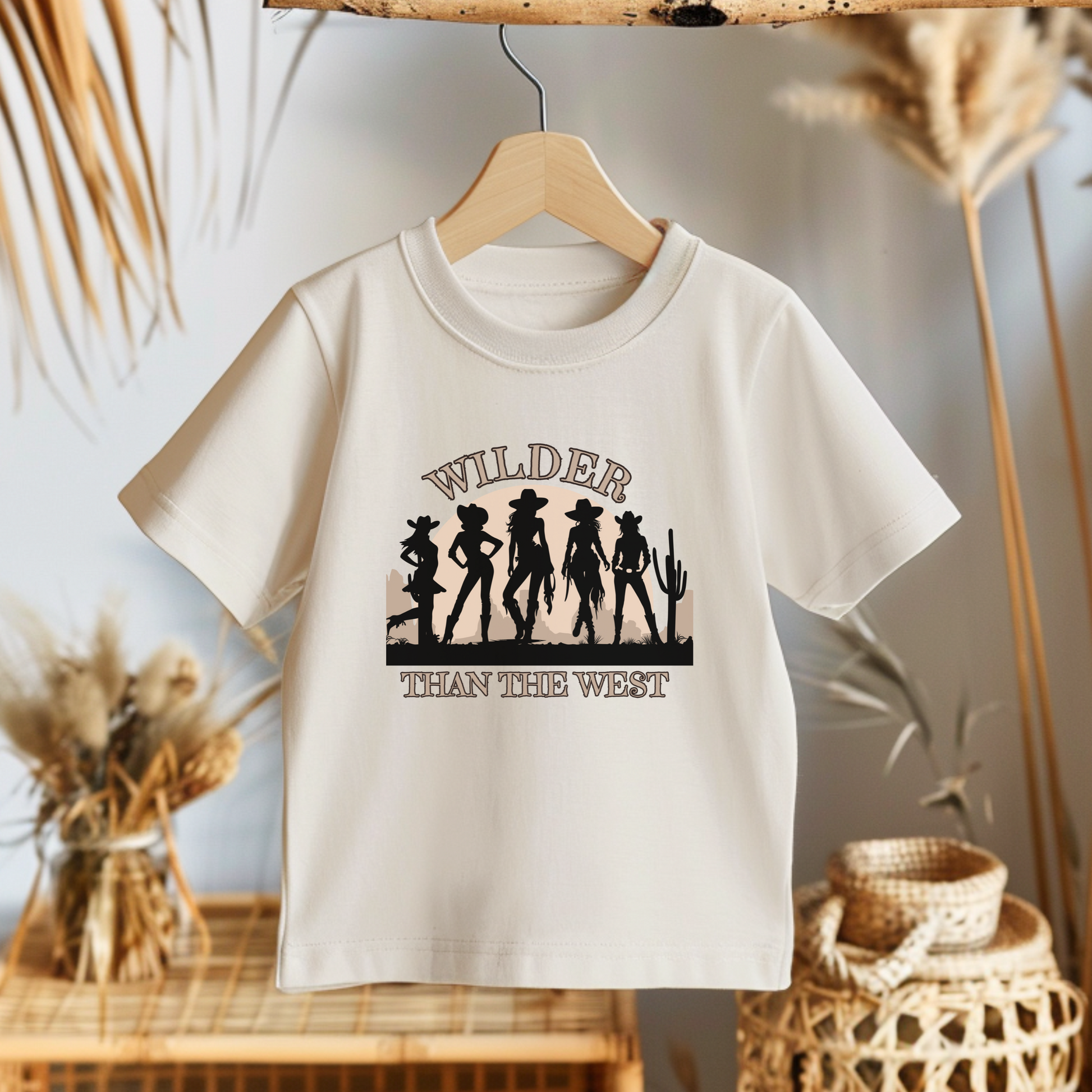 Celebrate your toddler’s bold spirit with this Wilder than the West cowgirl shirt. Featuring western silhouettes, a cactus scene, and soft natural color, it’s the perfect toddler tee for state fair days, Texas bachelorette weekends, or mama mini matching rodeo looks. A fun and empowering toddler quote shirt for girls who love horses, country music, and dressing up in southern coquette style.