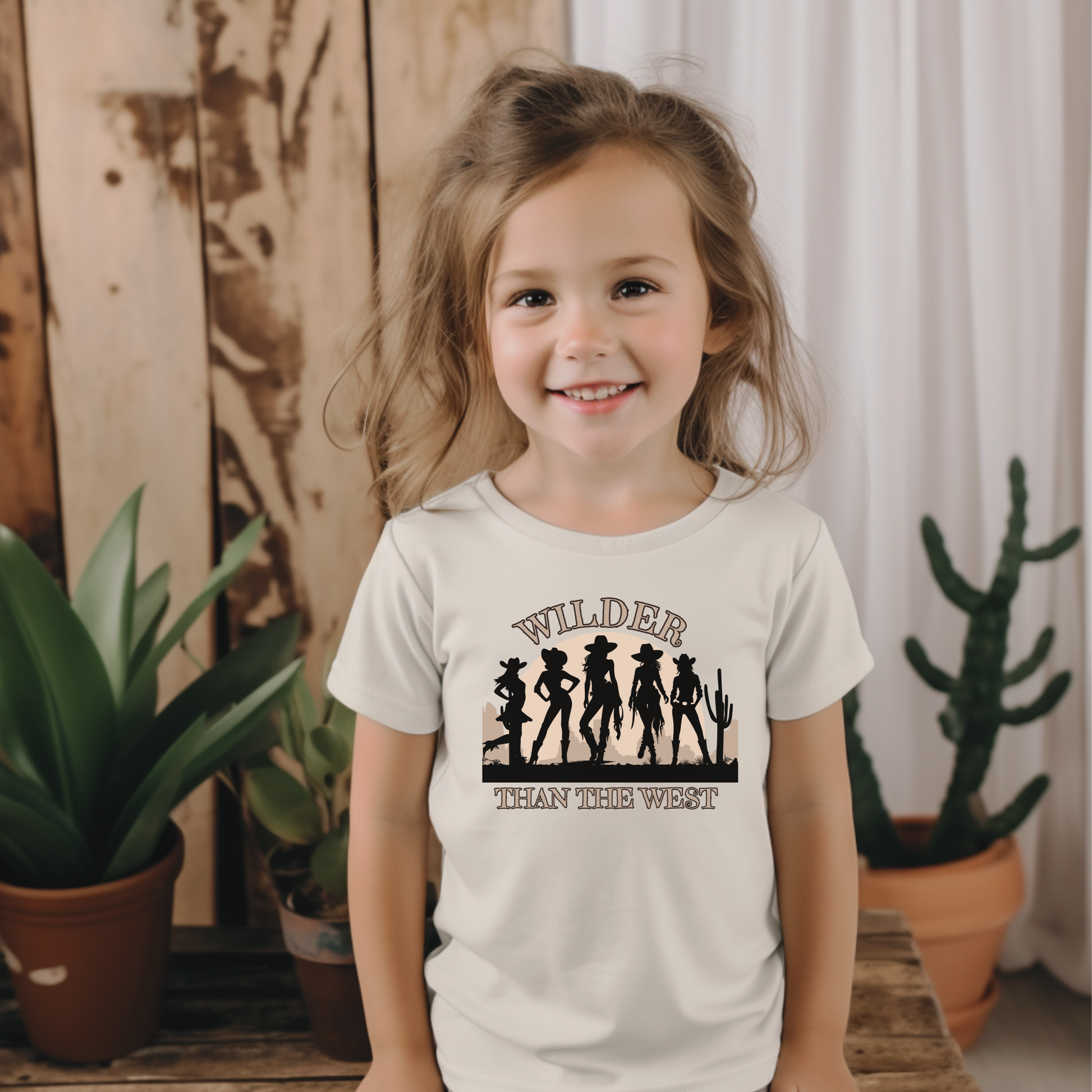 This toddler-sized Wilder than the West shirt features five strong cowgirl silhouettes, a glowing sunset, and desert cactus. Perfect for southern girls, rodeo-loving toddlers, or matching bachelorette party trips. A standout pick for toddler girls’ fair outfits or music fest weekends with mom. This western cowgirl silhouette tee comes in toddler sizes and coordinates perfectly with girls’ and women’s styles.