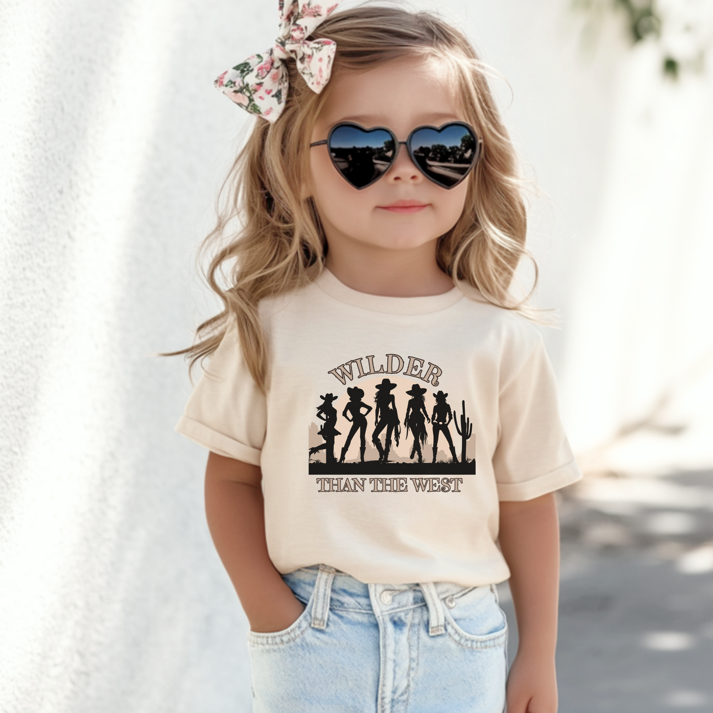 Wilder than the West toddler shirt in natural color featuring five cowgirl silhouettes, a desert sunset, and cactus design. This toddler western silhouette tee is part of a mommy and me match set for toddlers, girls, and women. Perfect for country girl birthday outfits, rodeo festivals, or state fair fun. A soft, comfy pick for southern, coquette, or coastal cowgirl style. Great for mini horse lovers and music fest family outfits.

