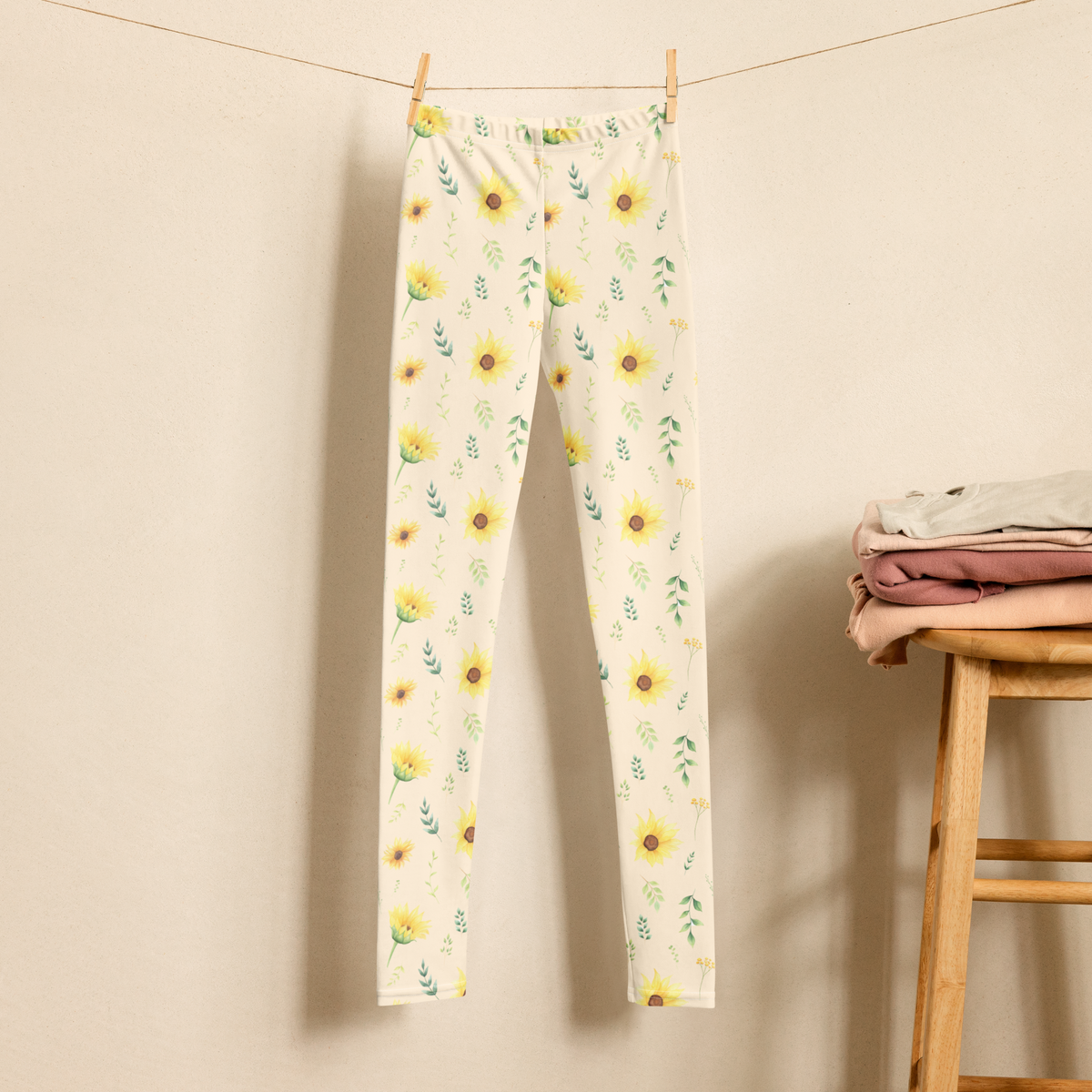 Girls leggings with a cottagecore inspired floral design featuring yellow sunflowers, green botanical leaves and delicate flowers scattered across a cream background. The print has the cheerful feeling of a country garden or wildflower meadow and works well for girls who love nature inspired clothing. The high rise full length leggings can be worn for school, playtime, family outings, vacations or relaxed spring and summer days.