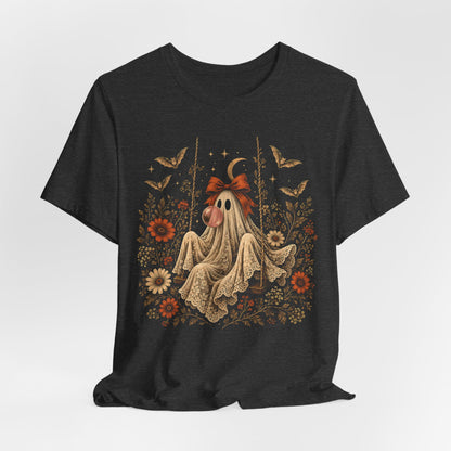 Bubble gum ghost Halloween shirt for women featuring a whimsical ghost sitting on a swing and blowing a bubble. Vintage flowers, botanical elements, bats, lace and a crescent moon surround the character in a playful spooky season design.