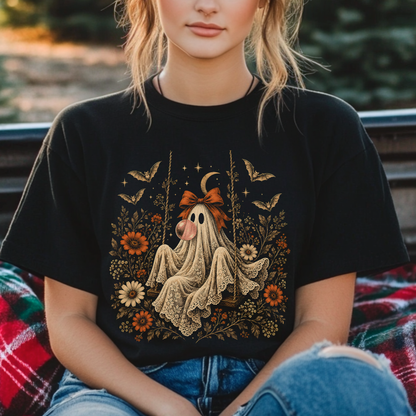 Women's vintage Halloween graphic tee featuring a playful ghost on a swing blowing bubble gum. Floral and botanical elements surround the ghost along with bats, lace, stars and a crescent moon for a whimsical spooky fall aesthetic.