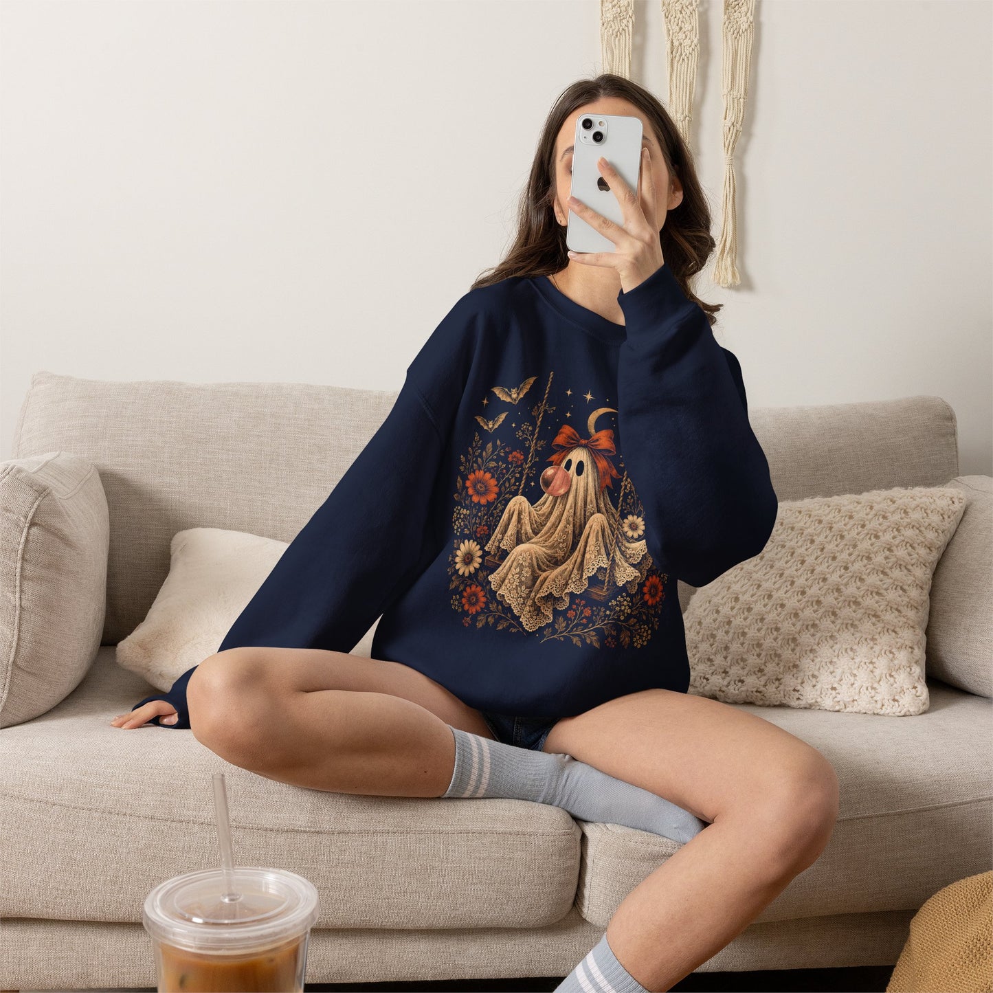 Women's vintage ghost Halloween sweatshirt featuring a playful ghost seated on a swing and blowing a bubble with bubble gum. The detailed artwork includes floral accents, botanical elements, bats, lace and a crescent moon for a whimsical spooky season aesthetic.