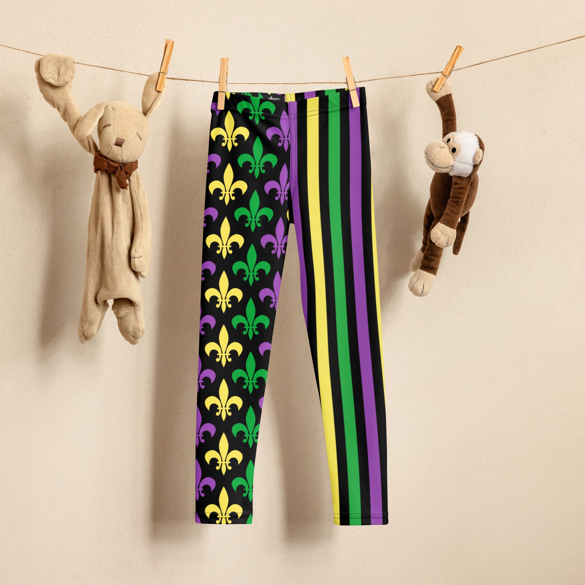 Mardi Gras Stripes and Fleur de Lis Kid's Leggings, size 2T-7. Black leggings featuring a fleur de lis pattern on one leg and vibrant green, purple, and yellow stripes on the other. Perfect for celebrating Mardi Gras, part of a matching collection including leggings for older children and women.