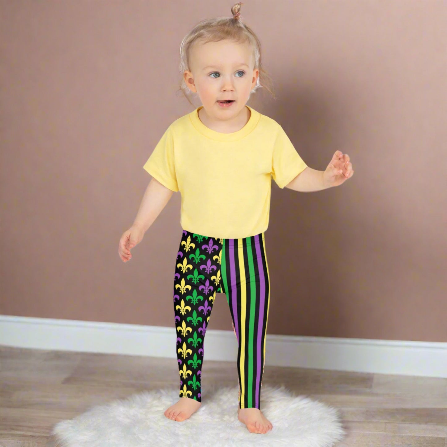 Mardi Gras Stripes and Fleur de Lis Kid's Leggings, size 2T-7. Black leggings featuring a fleur de lis pattern on one leg and vibrant green, purple, and yellow stripes on the other. Perfect for celebrating Mardi Gras, part of a matching collection including leggings for older children and women.