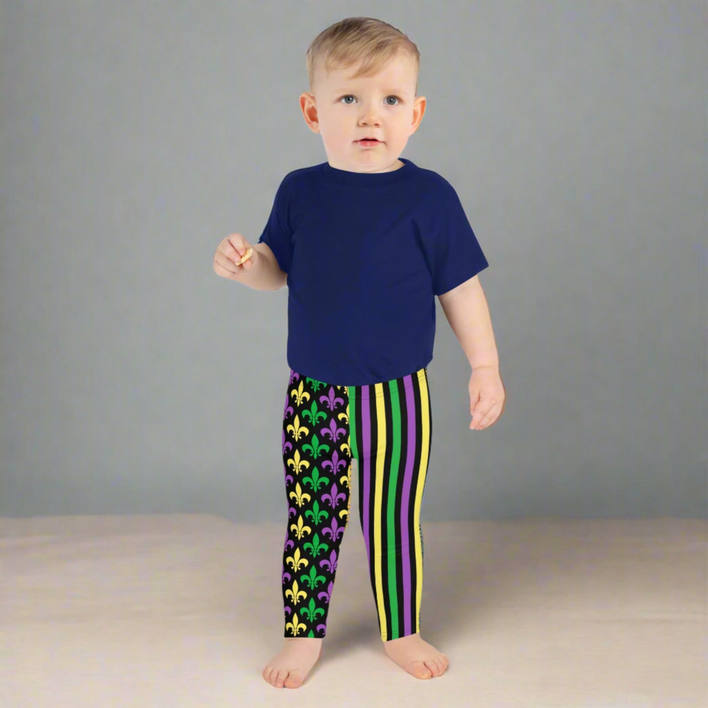 Mardi Gras Stripes and Fleur de Lis Kid's Leggings, size 2T-7. Black leggings featuring a fleur de lis pattern on one leg and vibrant green, purple, and yellow stripes on the other. Perfect for celebrating Mardi Gras, part of a matching collection including leggings for older children and women.