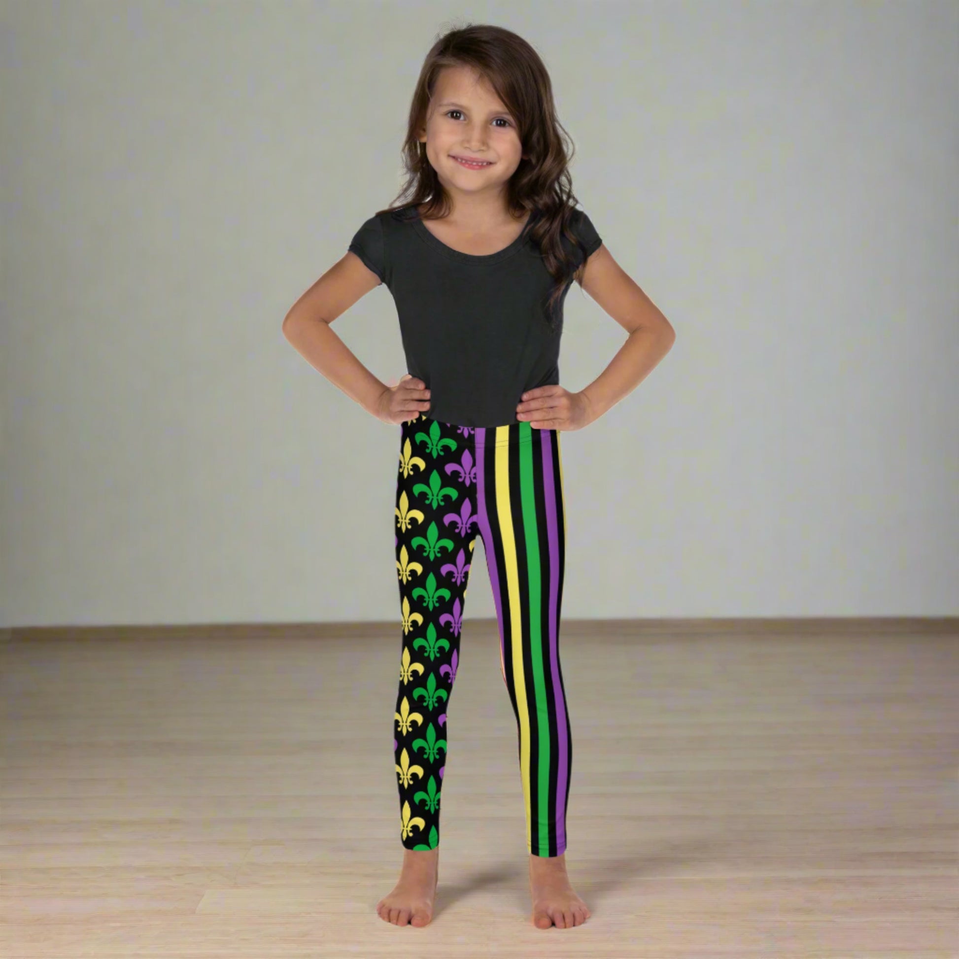 Mardi Gras Stripes and Fleur de Lis Kid's Leggings, size 2T-7. Black leggings featuring a fleur de lis pattern on one leg and vibrant green, purple, and yellow stripes on the other. Perfect for celebrating Mardi Gras, part of a matching collection including leggings for older children and women.