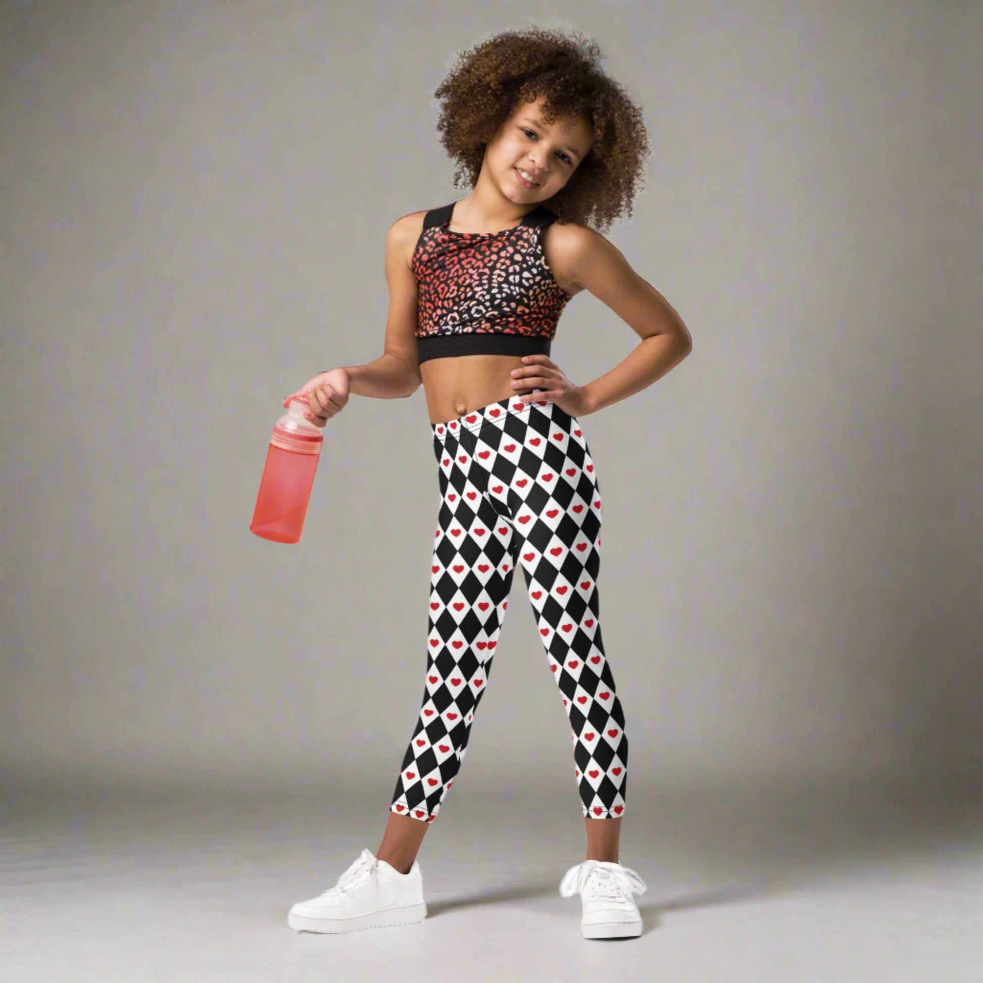 Image: Harlequin Love Girls Leggings in sizes 2T-7. These yoga tights have a black and white checker/ diamond pattern with a red heart accent, the perfect leggings for valentines day or a Queen of Hearts costume, by jaecrece