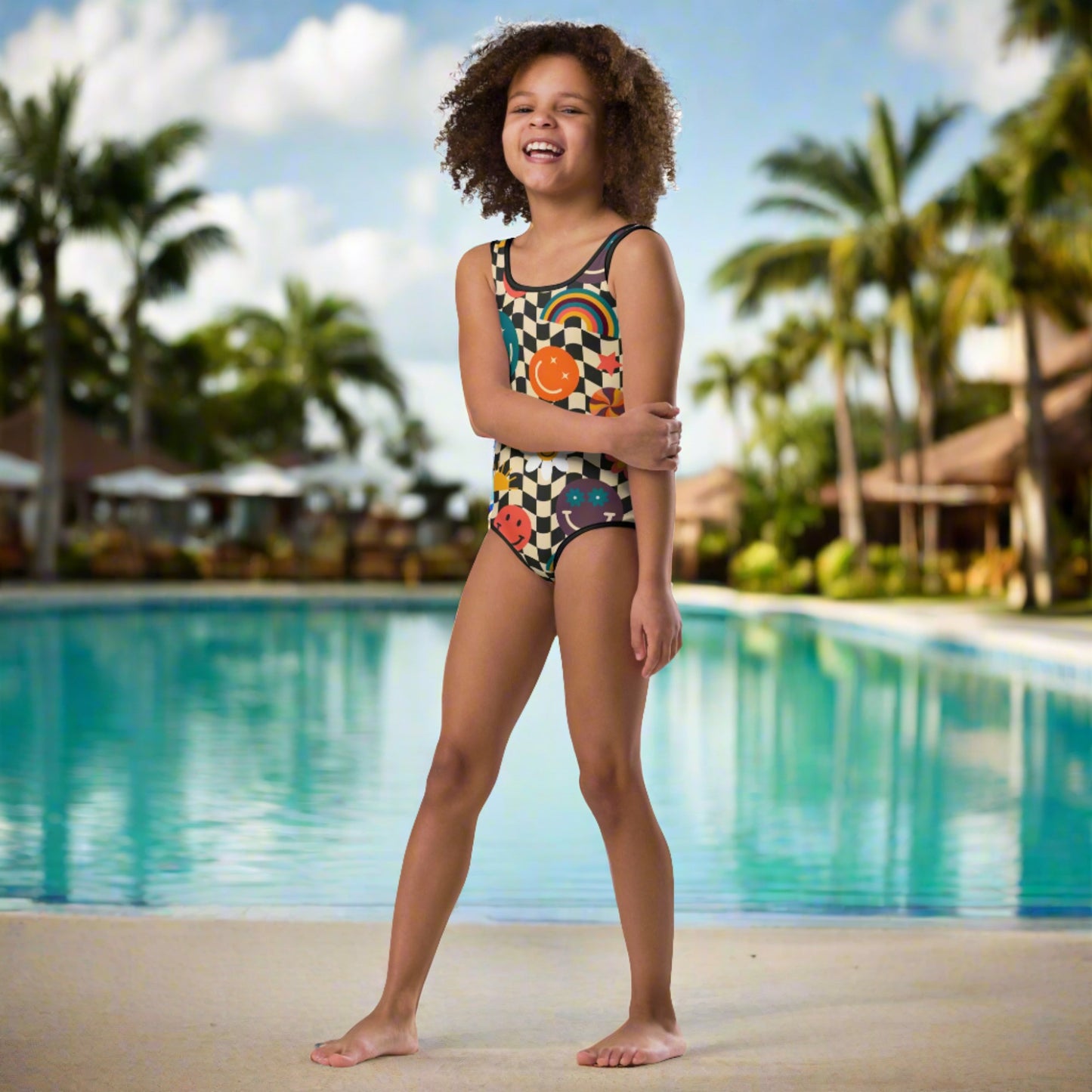 Smiley Face Checkerboard Girls One Piece Bathing Suit. This cute retro swimsuit features a black and khaki checkerboard background, with smiley face, rainbow and daisy graphics. In toddler and girls sizes, 2T-7. by jaecrece.com