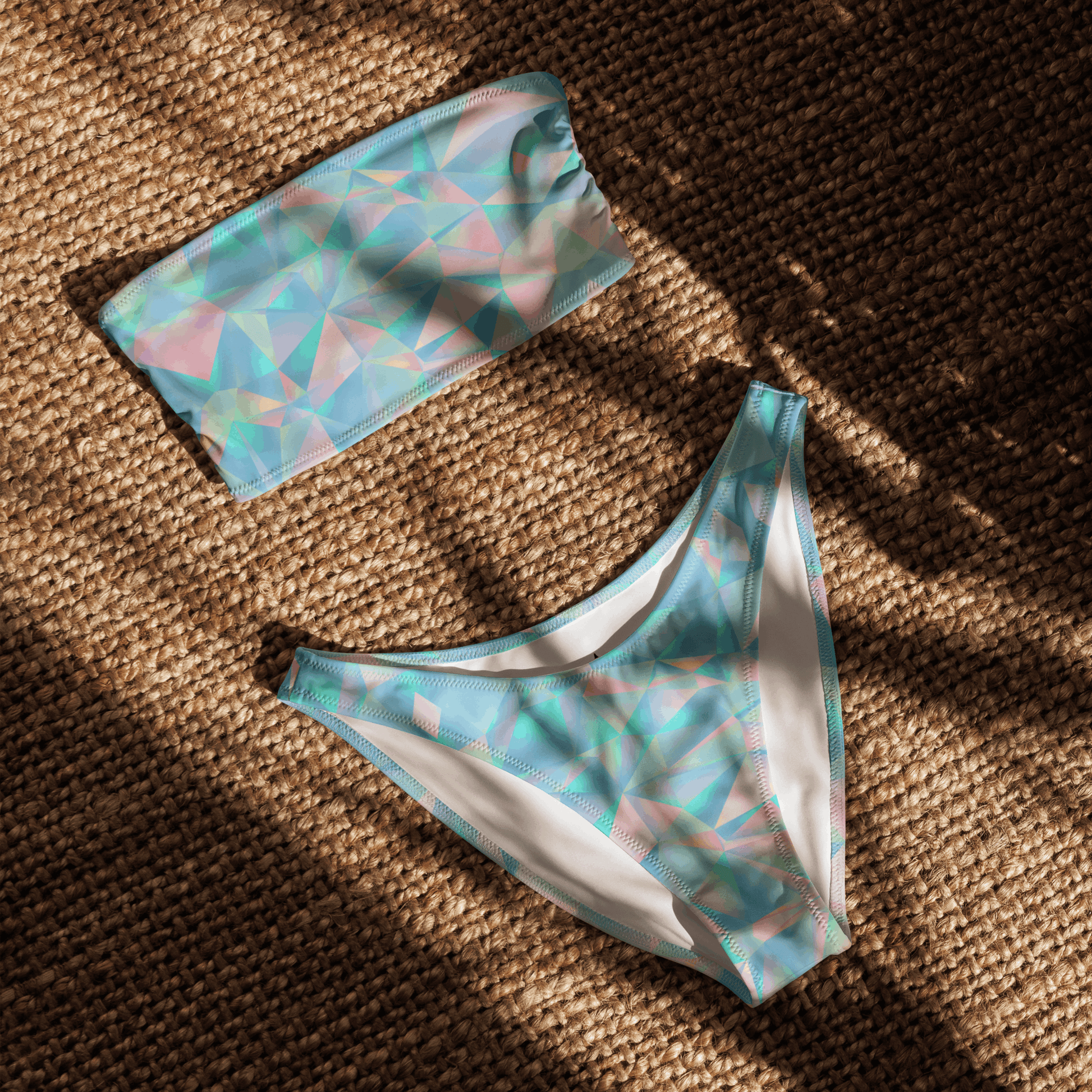 Flat lay of the Blue Prisms eco-friendly bandeau bikini set showing the strapless top and high-leg V-cut bottoms in a blue, teal, and pink geometric pattern. This sustainable swimsuit is made with recycled fabric, offering UPF 50+ sun protection and four-way stretch. Perfect for eco-conscious buyers, beach trips, and summer vacations. Sizes 2XS–6XL available. Custom printed swimwear, ethical fashion, and modern design.