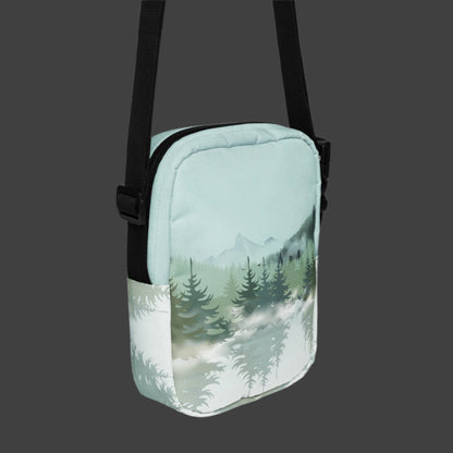 Image: Winter Forest Small Cross Body Bag. This nature inspired sling bag has an ombre snowy mountain print that fades from a blue gray sky to mountains and pine trees to white snow. This mini backpack has a zipper closure and two storage pockets for hands free outdoor adventures. Great for tween girls, teens and ladies, by jaecrece