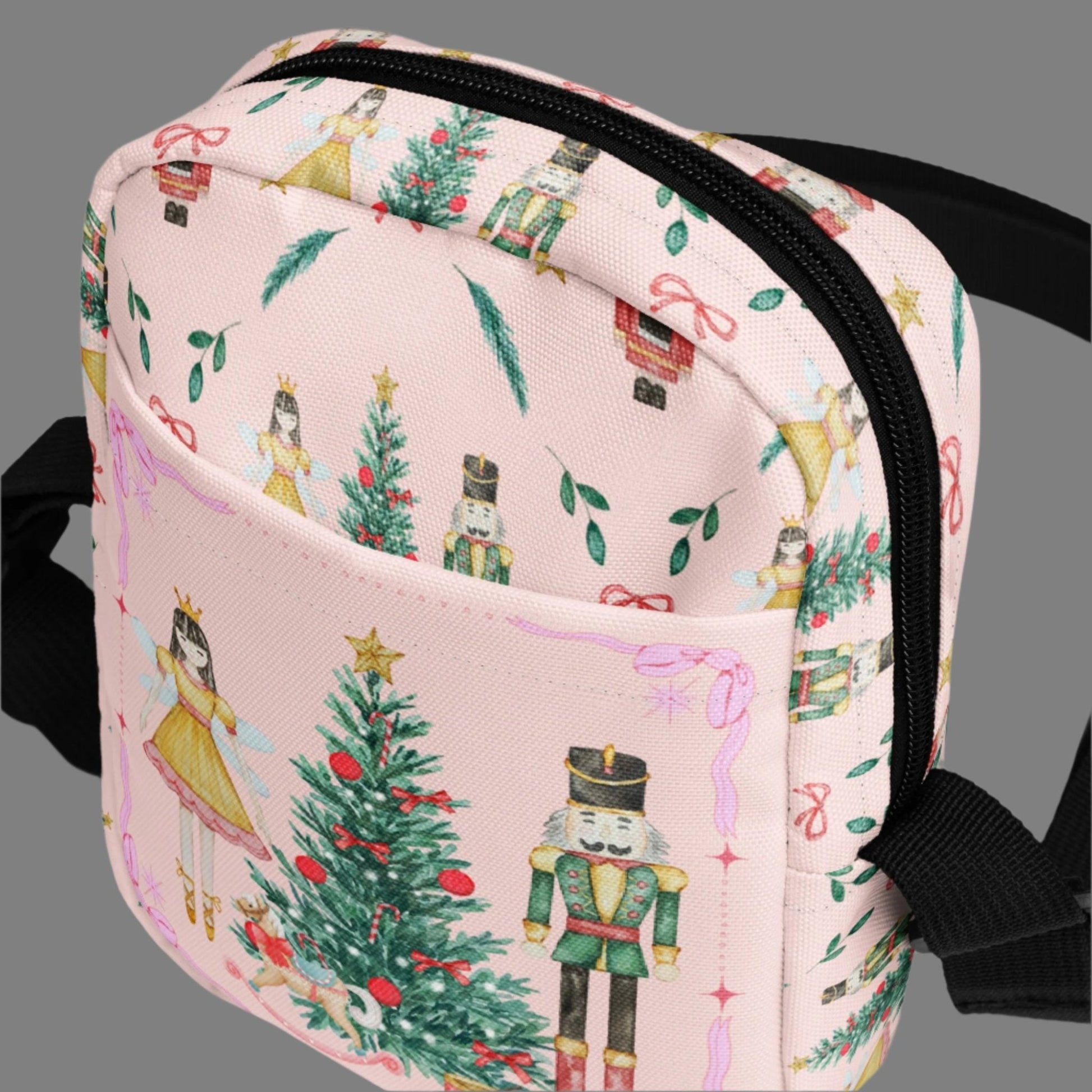 Image: Pink Coquette Nutcracker Utility Crossbody bag. The front of this small mini tote has a Christmas tree, Nutcracker, Sugarplum Fairy, Rocking Horse and a holiday present The rest of the purse is covered in a pattern of ribbons, garland, and Nutcrackers. May be worn across the waist/ hips, across the chest or as a mini backpack, by jaecrece